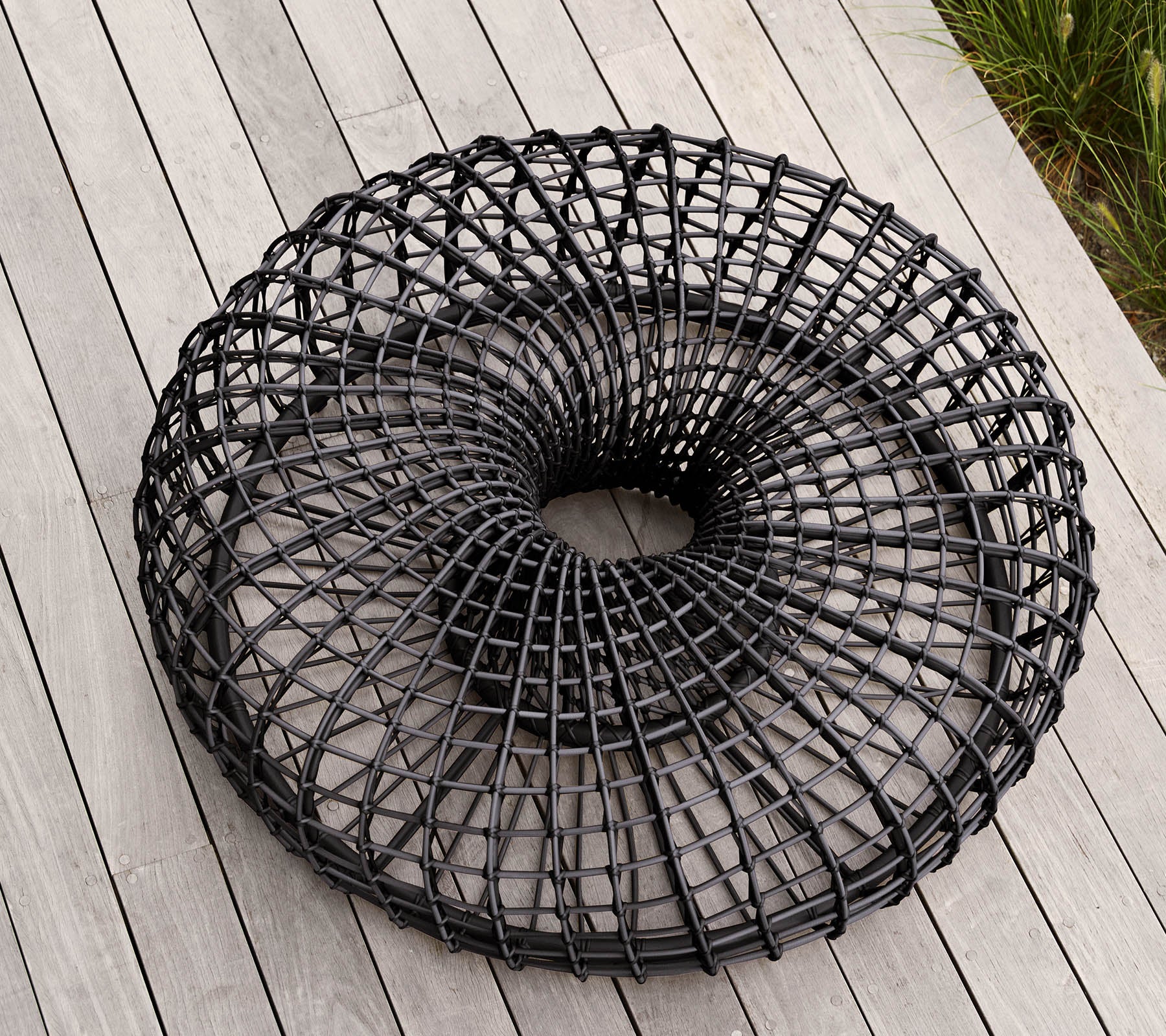 Moderne, sirkulær svart trådkurv med et unikt åpent vevdesign, som hviler på en flat overflate. Ideell for lagring eller dekorative formål.
