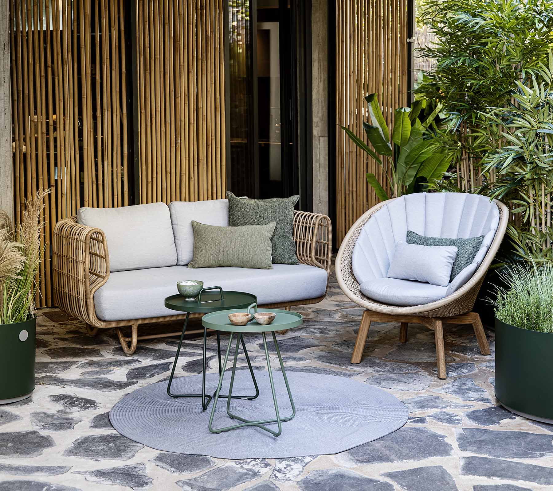 Et koselig sittearrangement med en rotting sofa og en stilfull stol, sammen med et lite bord og dekorative planter.