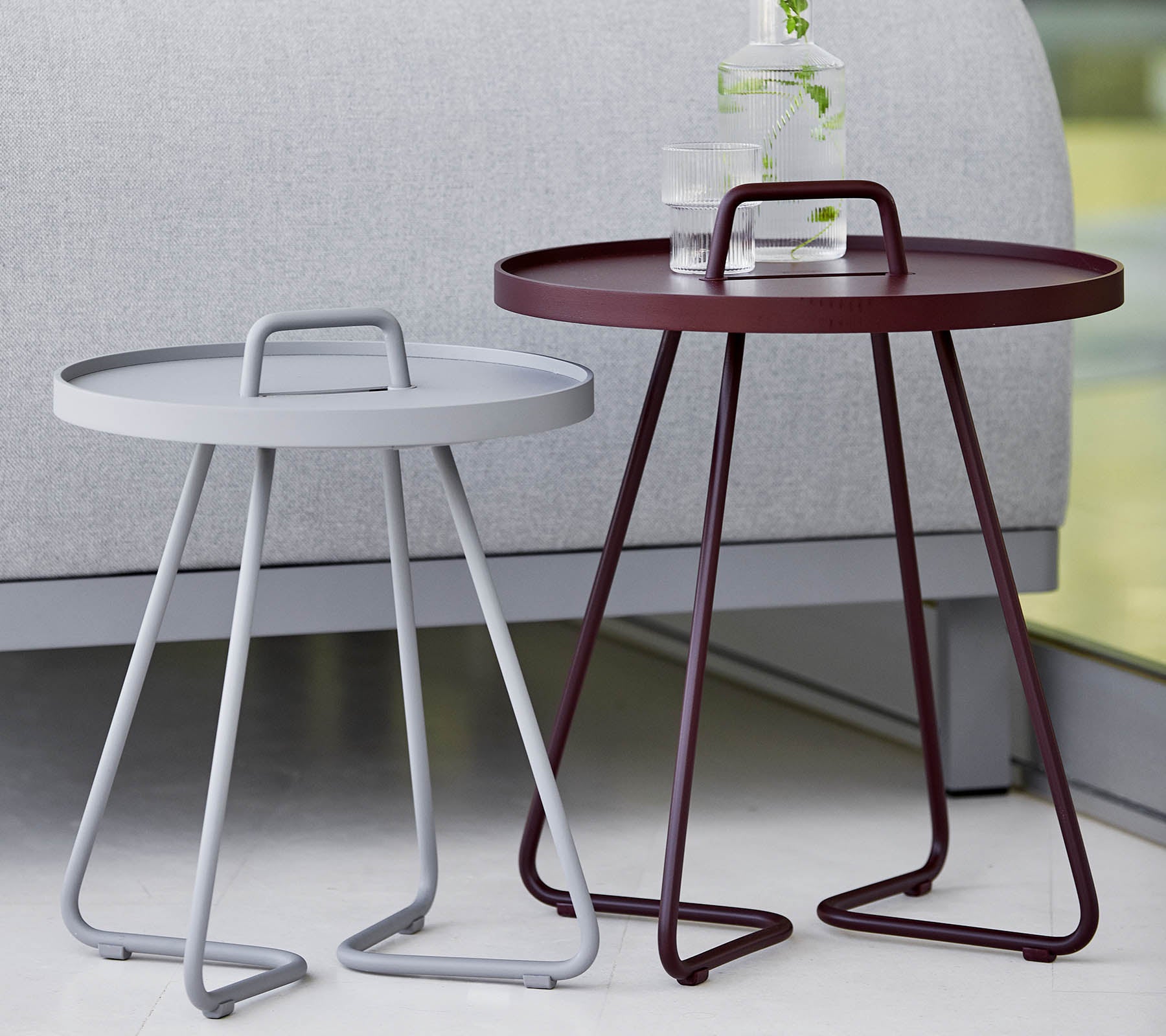 To moderne sidebord, ett grått og ett burgunder, begge med runde brett og stilige tripodben. Ideelle for moderne interiør.
