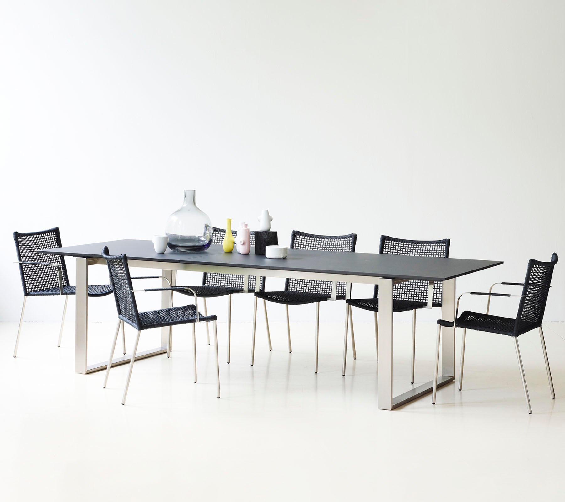Et moderne spisebord med et glatt design, omgitt av stilige svarte mesh-stoler og dekorative vaser.