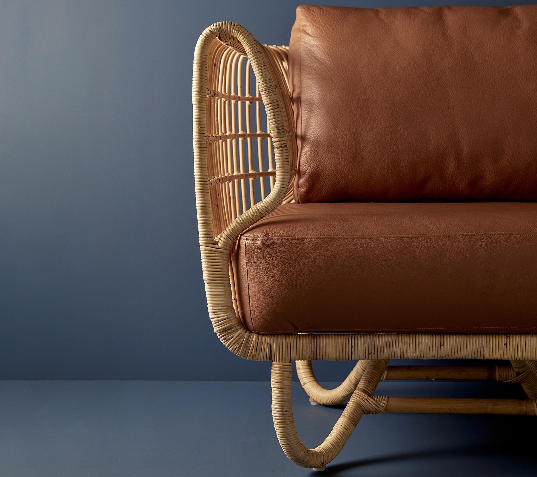 Rattanstol med en buet design og brune skinnputer, som viser en blanding av naturlige materialer og moderne estetikk.