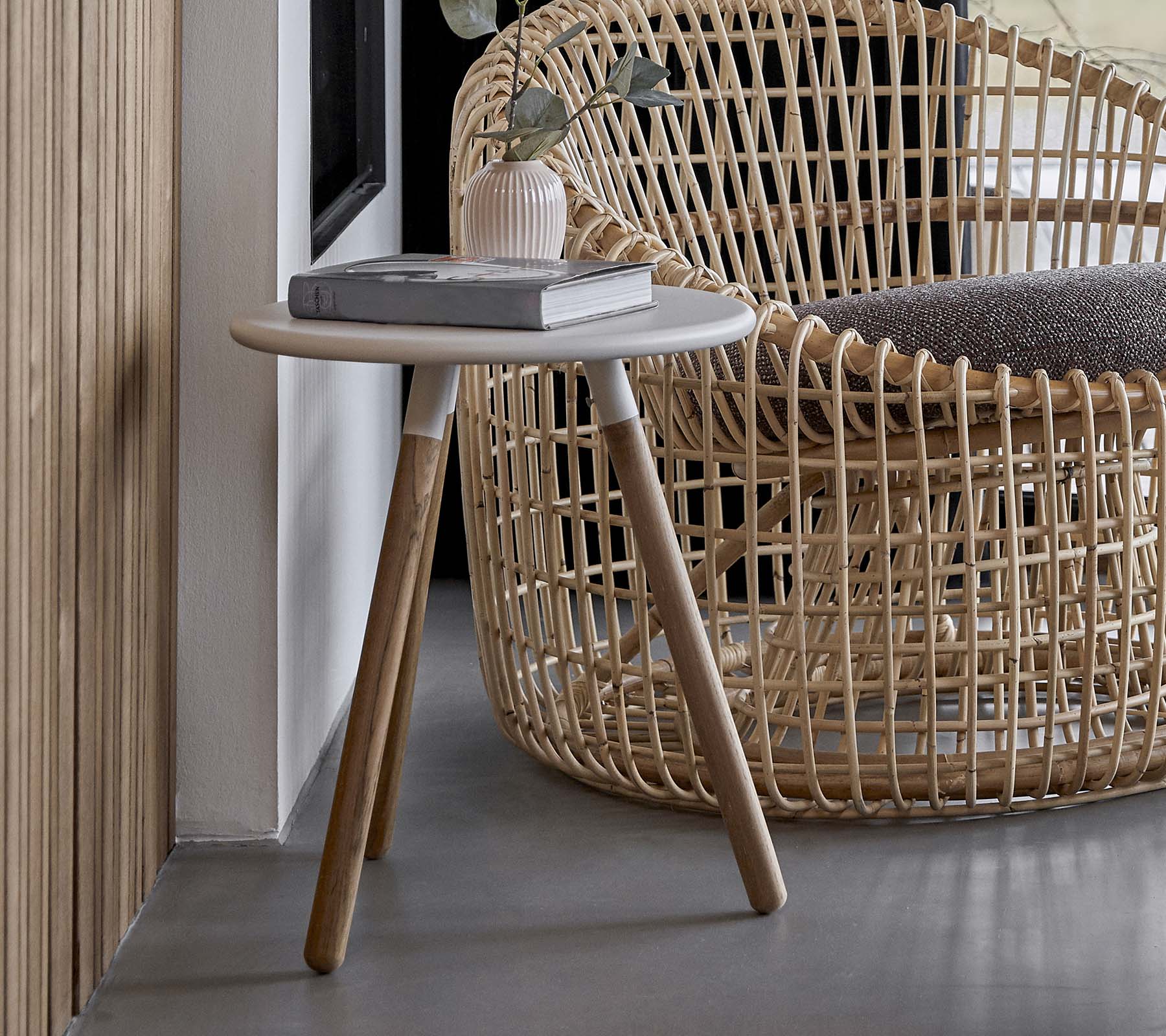 Et rundt sidebord med en lys overflate og tremmer, plassert ved siden av en vevd stol.