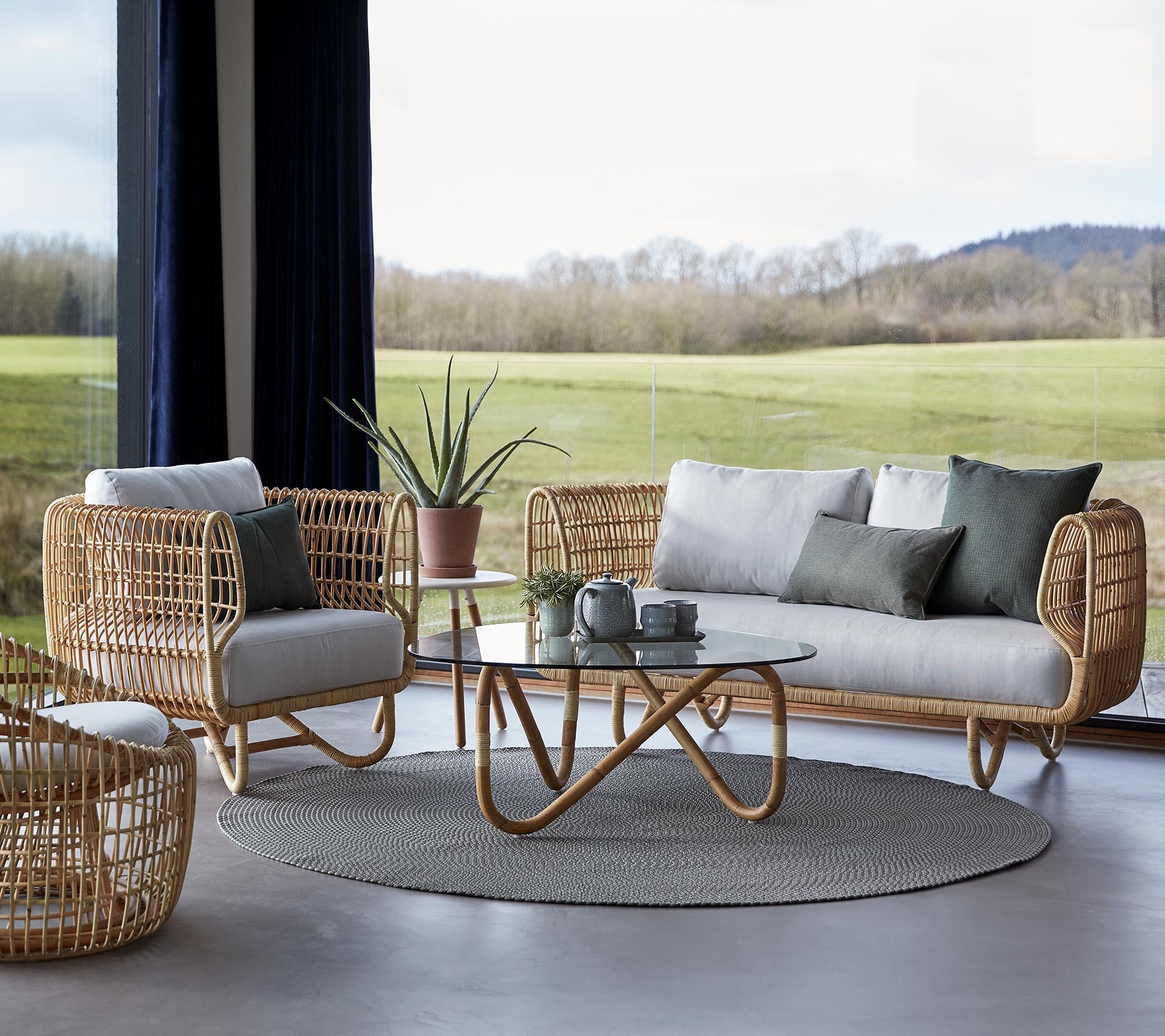Et stilfullt sittearrangement med flettede møbler, et rundt teppe og et glassbord, komplementert med minimalistiske dekorative elementer.