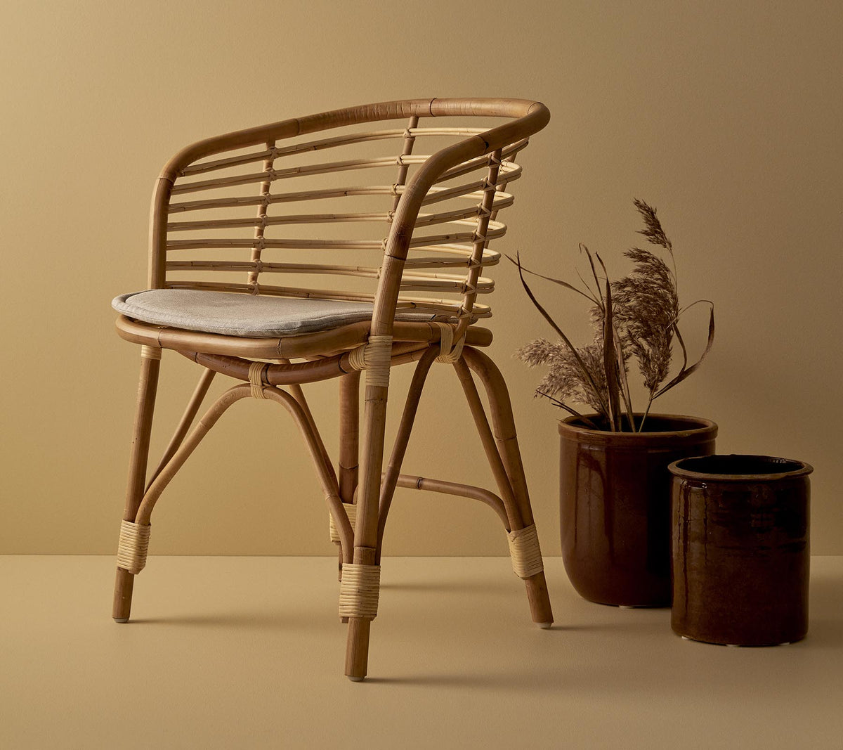 En stilfull rattan stol med polstret sete, ledsaget av to dekorative plantekasser med tørkede planter.
