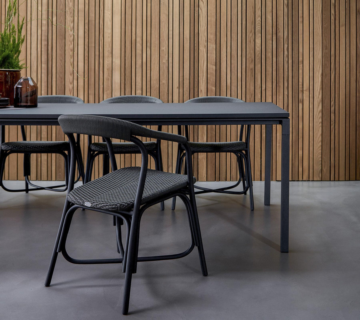Et moderne spiseområde med et stilrent bord omkranset av stilige stoler, mot en teksturert trevegg.