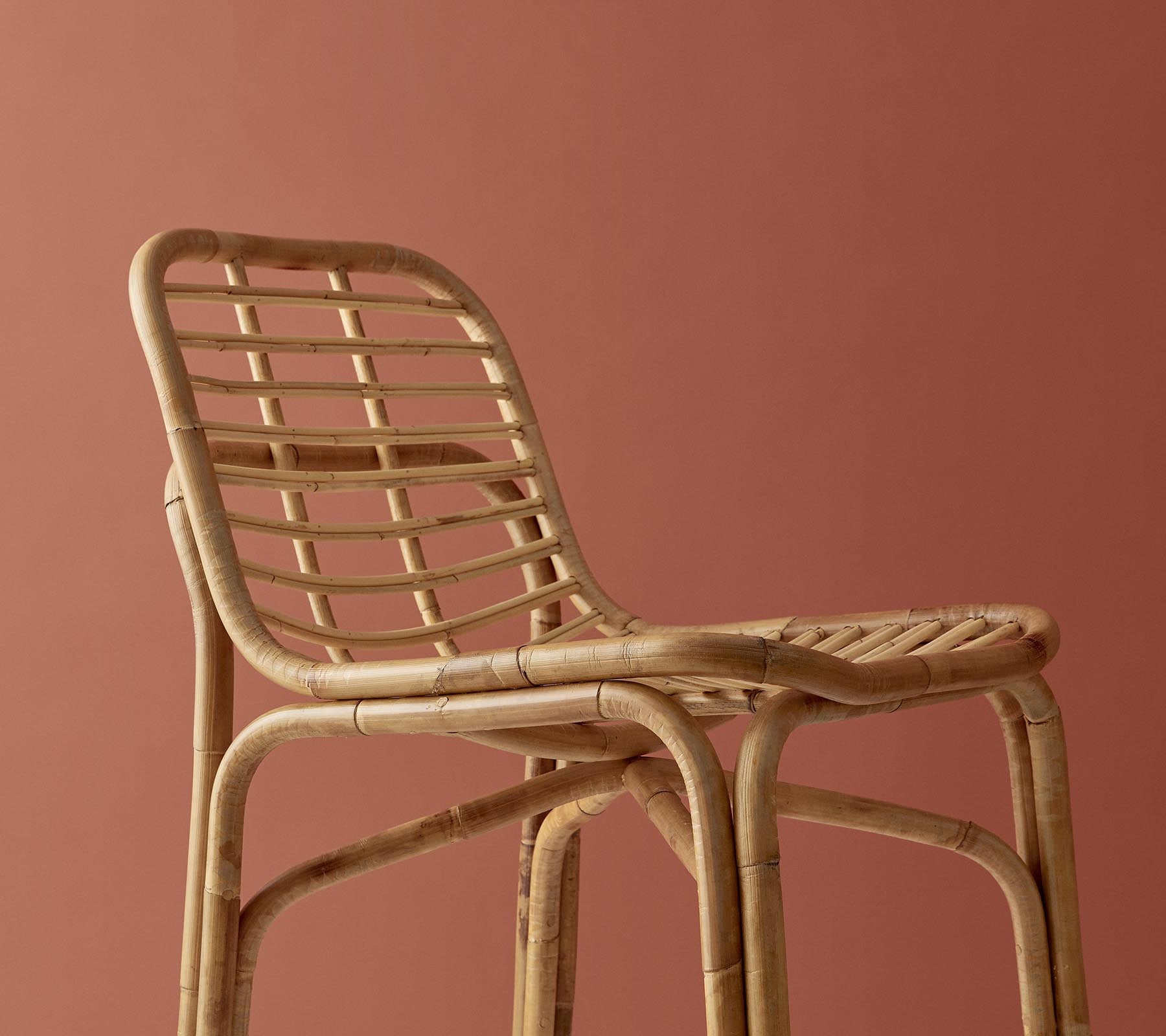 Stilig vevd stol med en naturlig finish, som har et minimalistisk design mot en dempet bakgrunn.