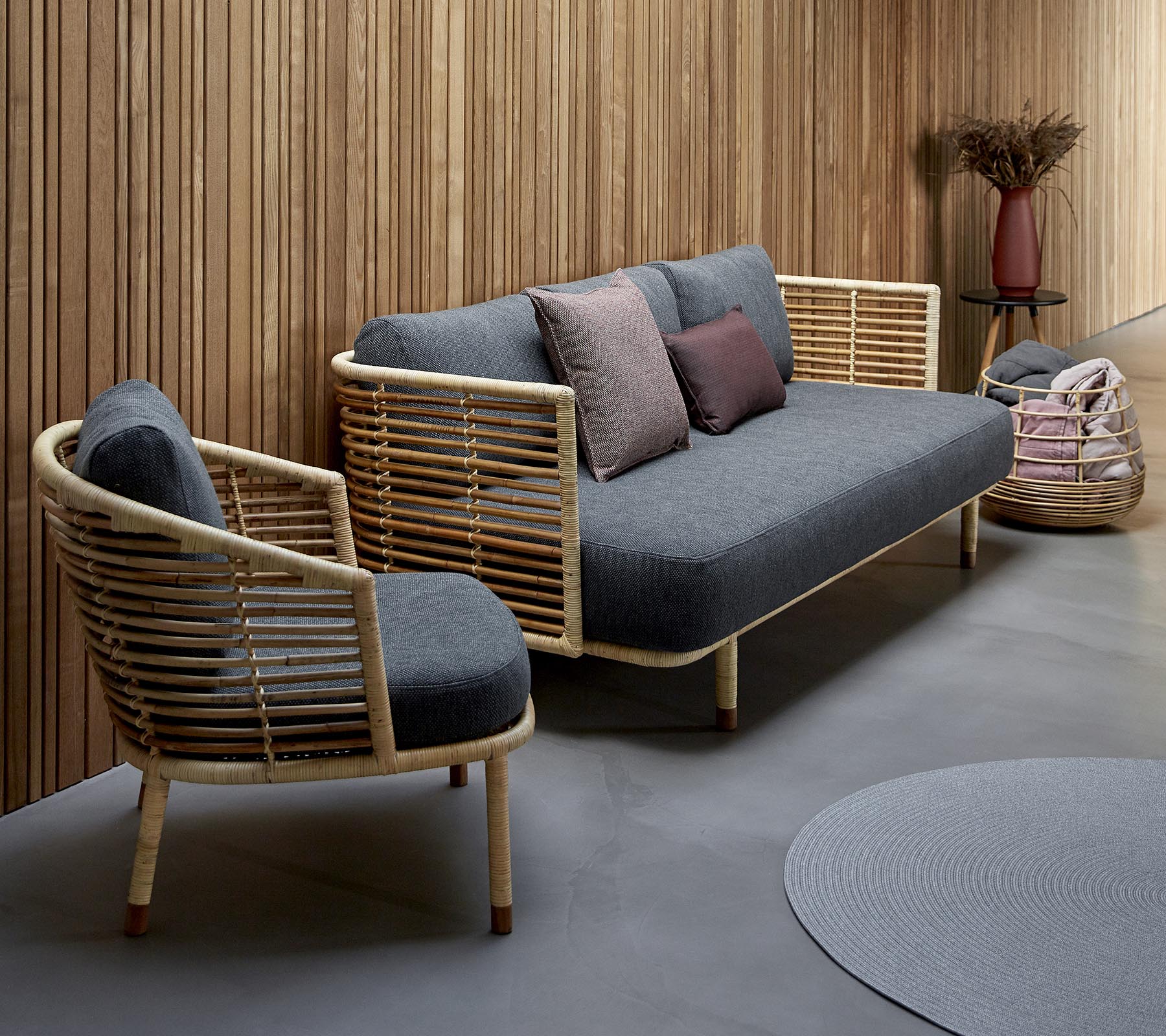 Stilig sittearrangement med en grå polstret sofa med treakenter og en matchende stol, supplert med dekorative puter.