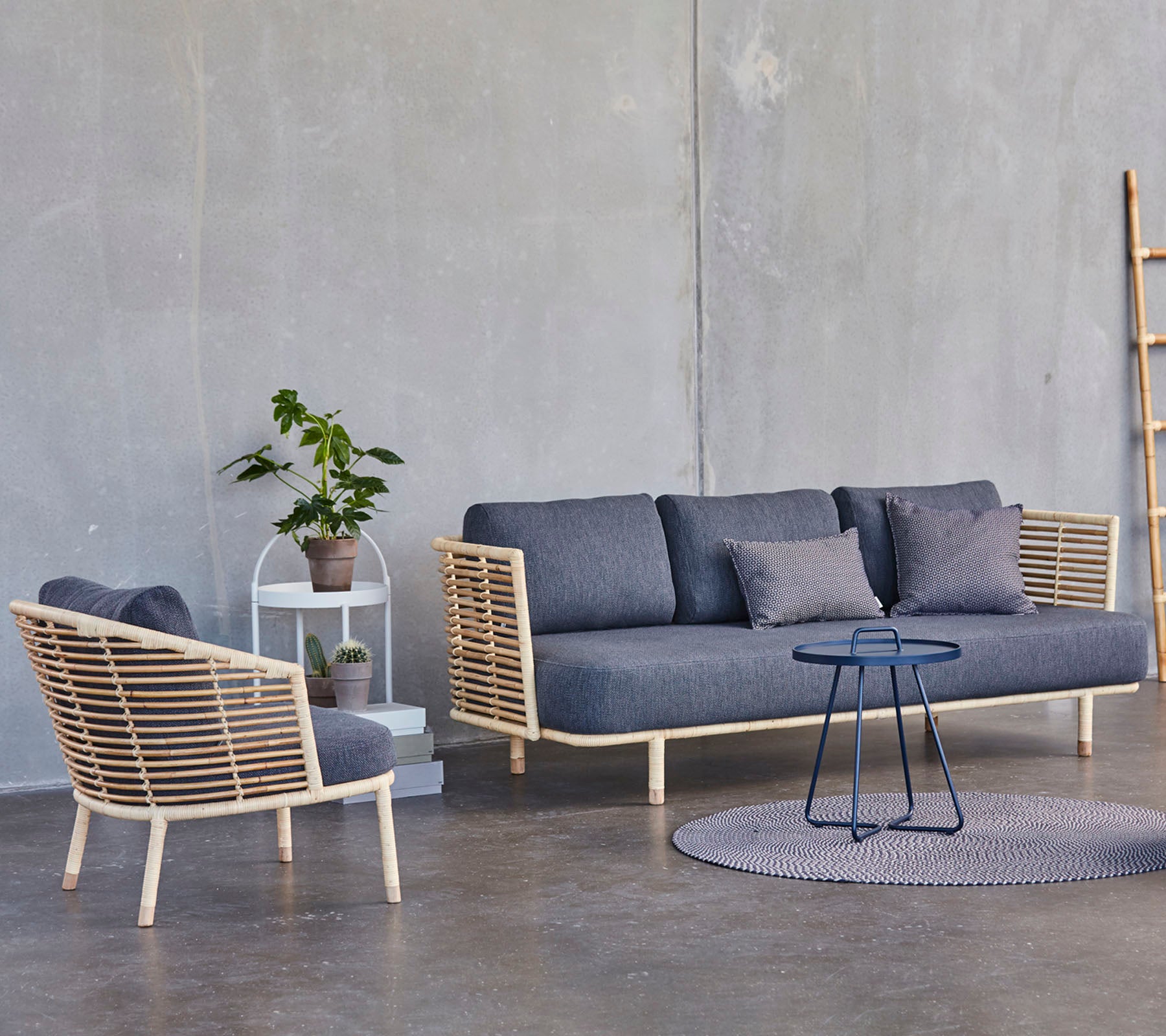 En moderne sitteordning med en stilfull sofa og lenestol med tre detaljer, sammen med et lite sidebord og en potteplante.
