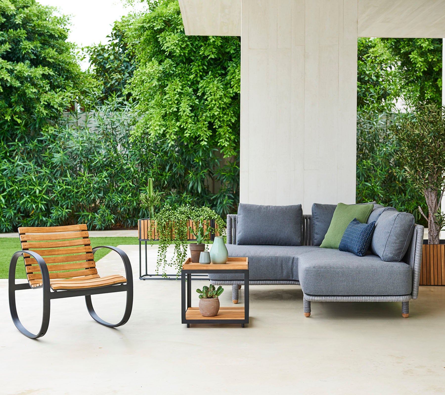 Moderne sittearrangement med en modulsofa med puter, en stilfull stol og et sidebord med dekorative planter.