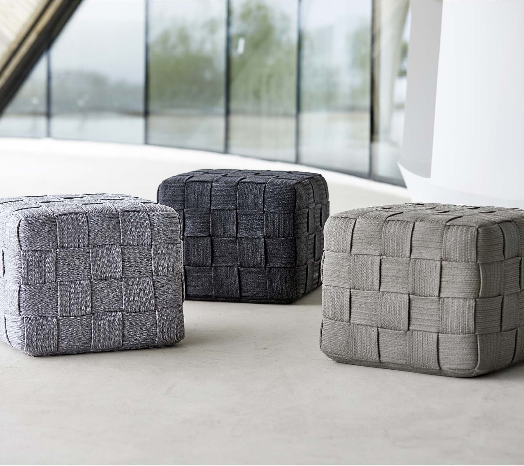 Tre vevde poufer i varierende grånyanser, med et teksturert design, plassert på en lys overflate. Ideelle for sitteplasser eller dekor.