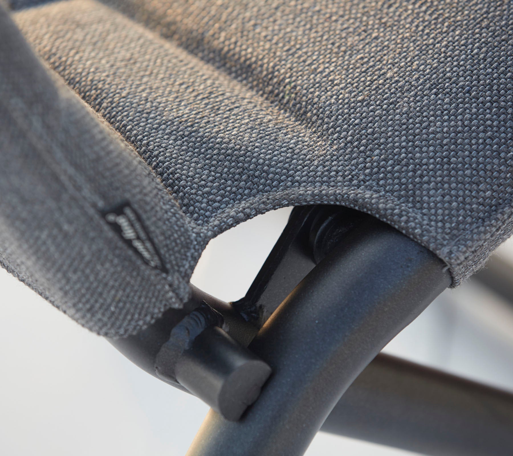 Nærbilde av en stol med teksturert stoffsete og solid svart ramme, som fremhever søm og designdetaljer.
