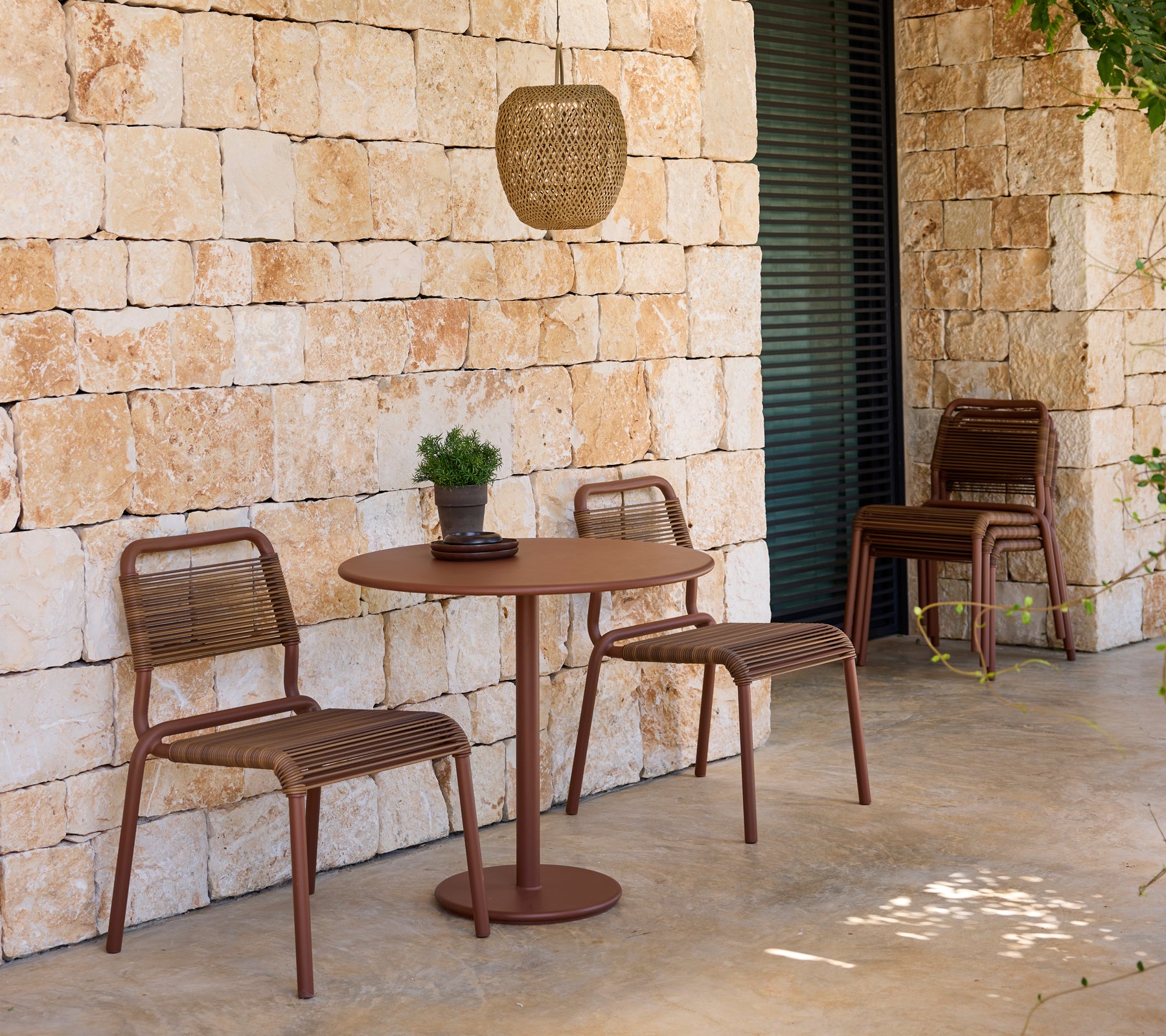 Moderne utendørs sitteplasser med brune stoler og bord mot en steinvegg.