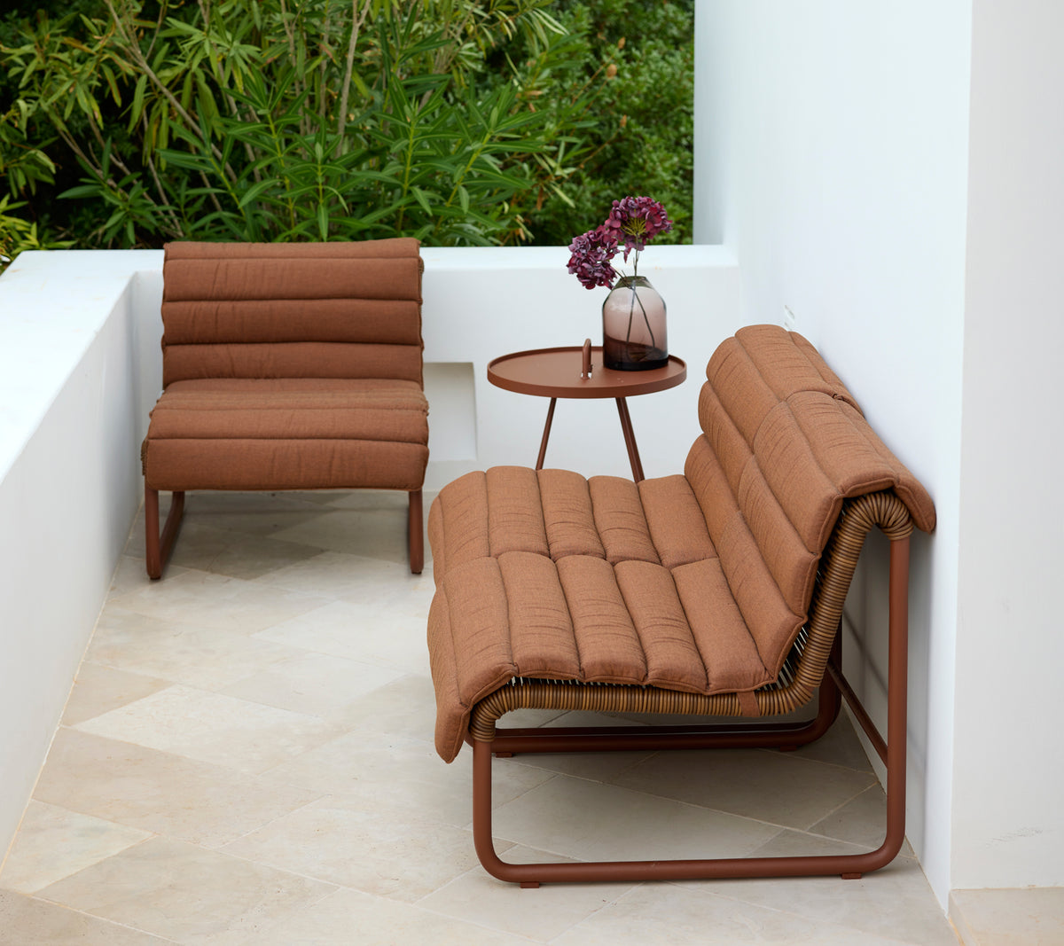Brun lenestol og loveseat med et rundt sidebord i en moderne utendørsinnstilling.