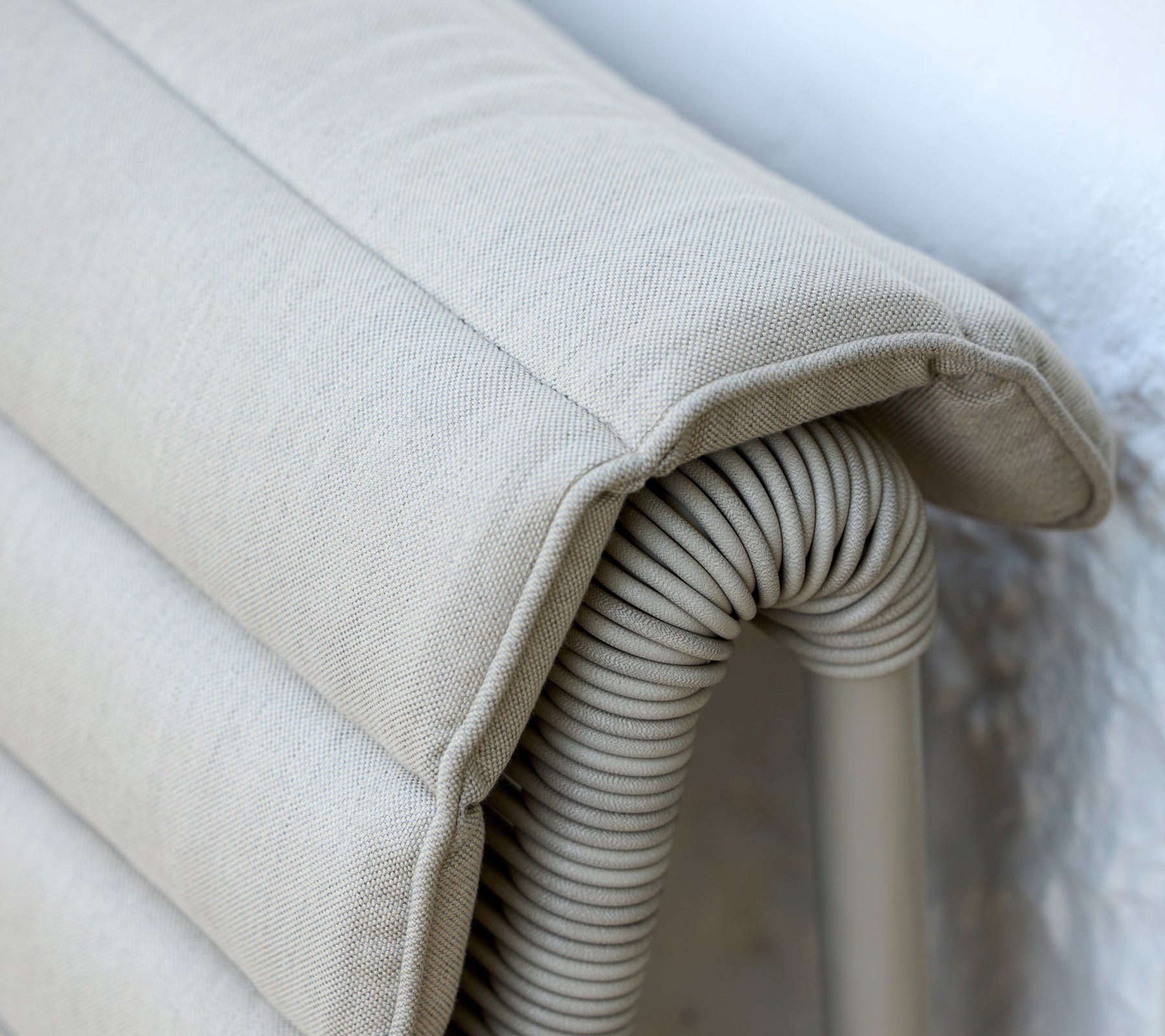 Beige pute med ribbet tekstur som hviler mot en lys vegg.