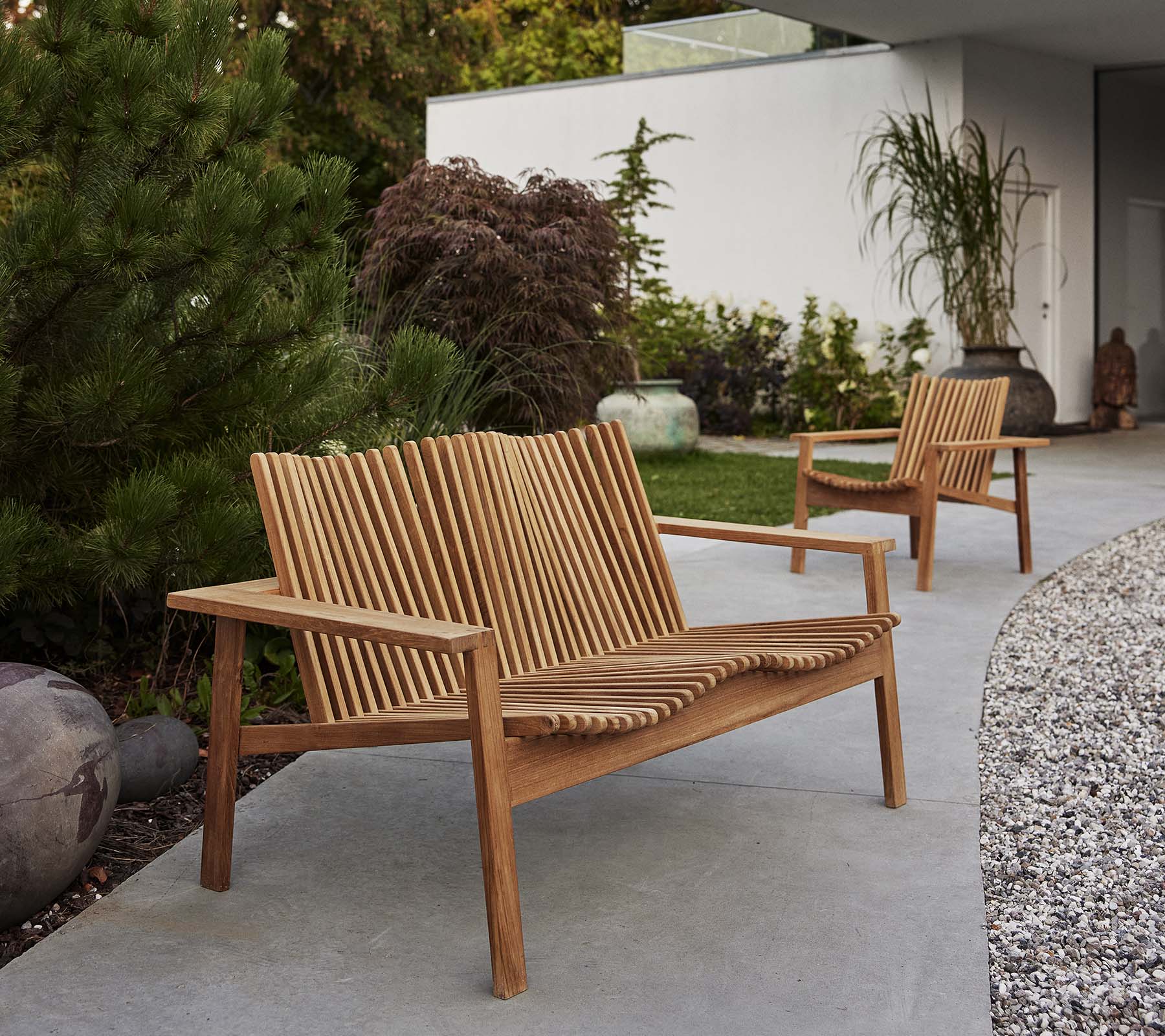 To treverk Amaze-loungestoler og en matchende sofa har et spaltet design, omgitt av grønt og dekorative elementer.