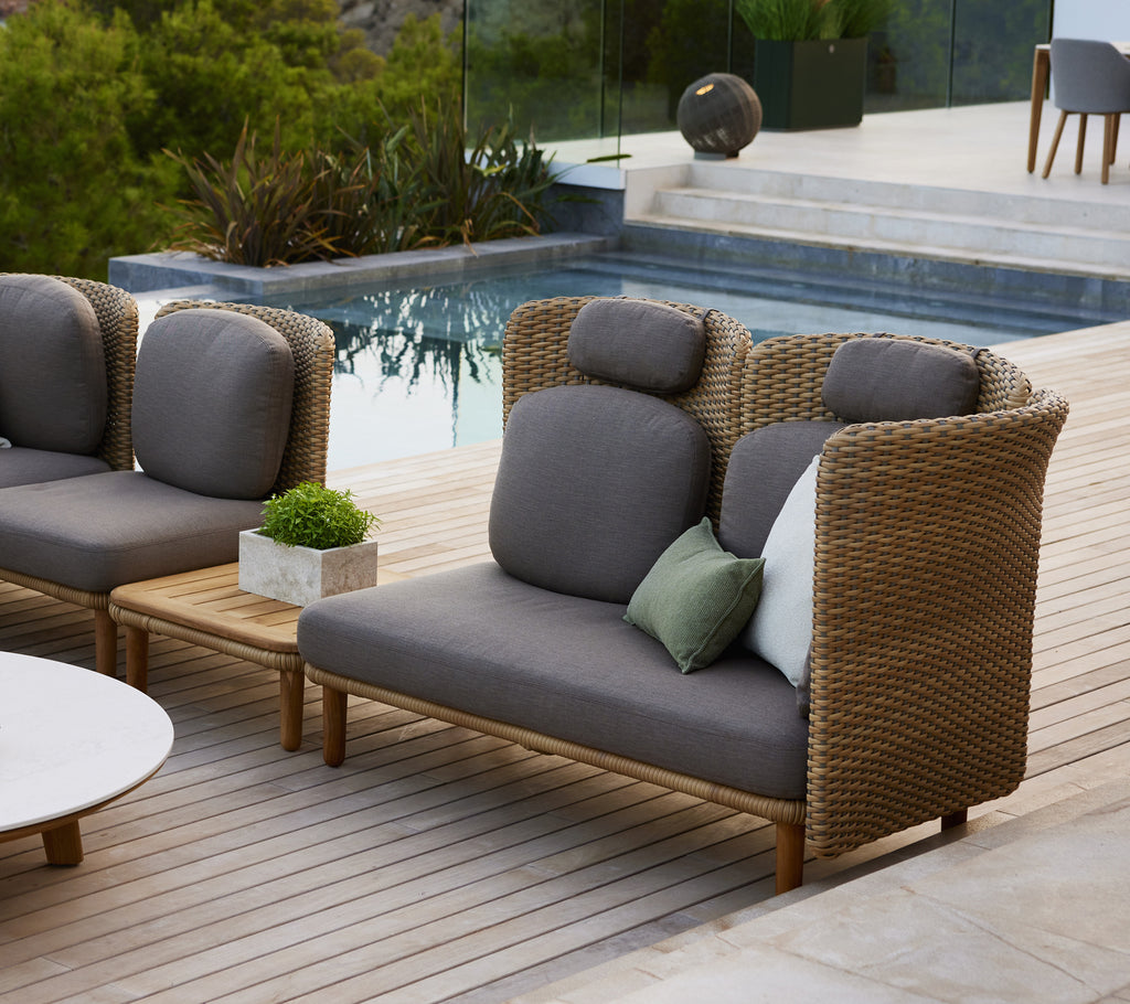 Stilig sofa med høy rygg og buede armlener, med grå puter og en blanding av dekorative puter på et treflo.