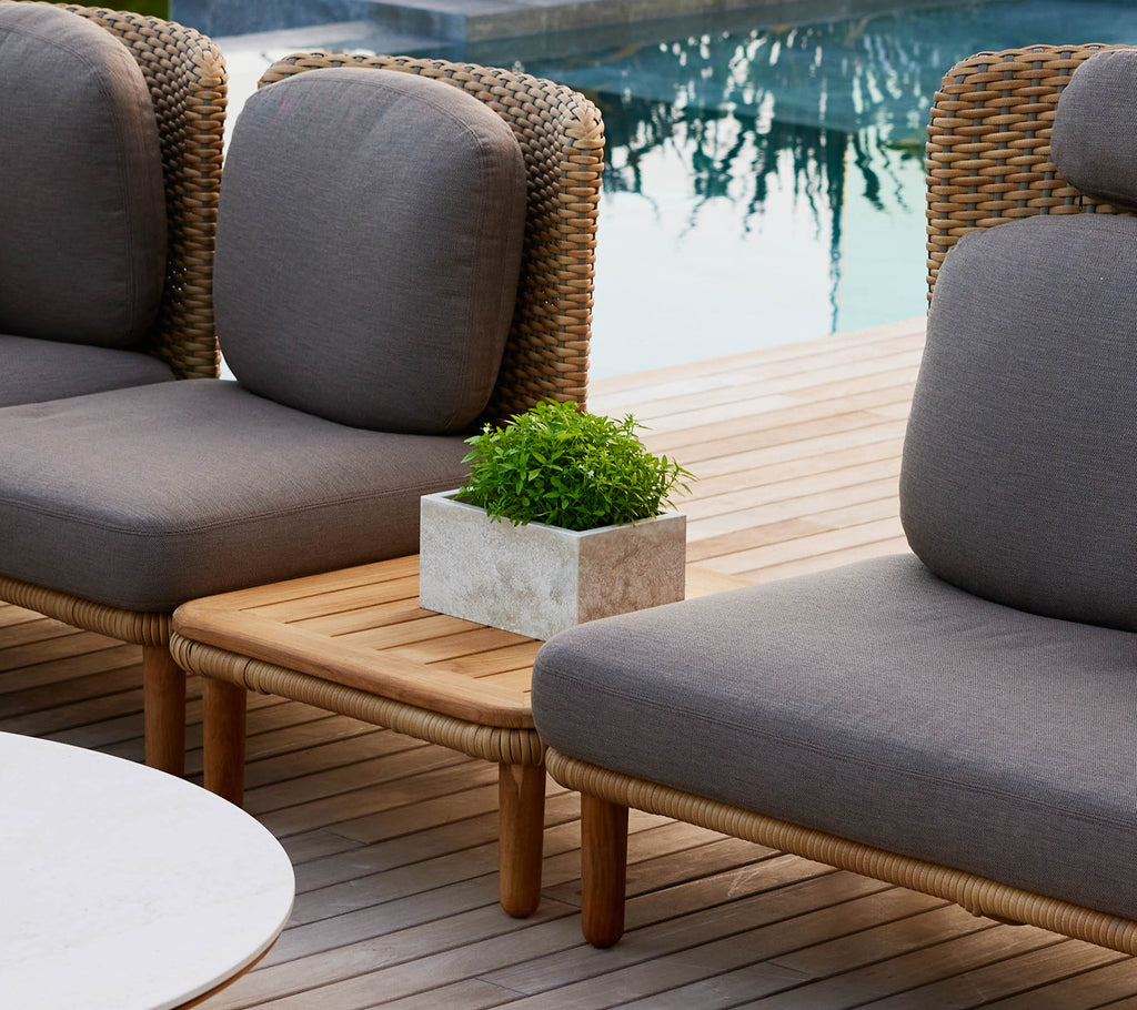 Et stilig Arch kaffebord med en teakplate, flankert av lounge stoler og en liten potteplante, som forbedrer en chic utendørs setting.