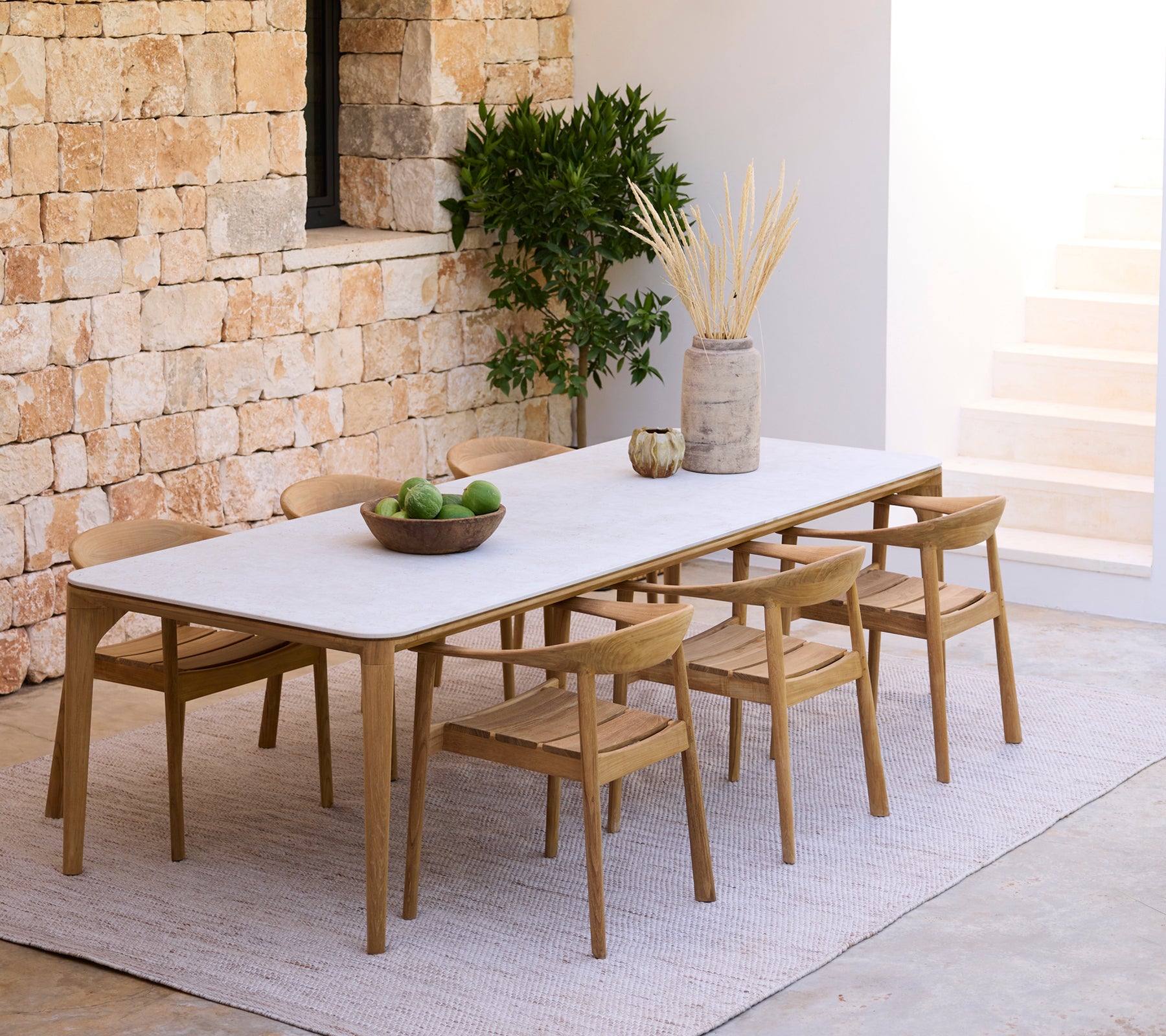 Moderne spiseoppsett med et hvitt bord og tresstoler mot en steinvegg.
