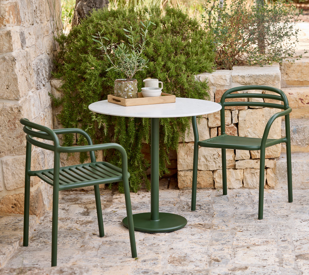 Moderne utendørs setting med grønne stoler og et hvitt bord.