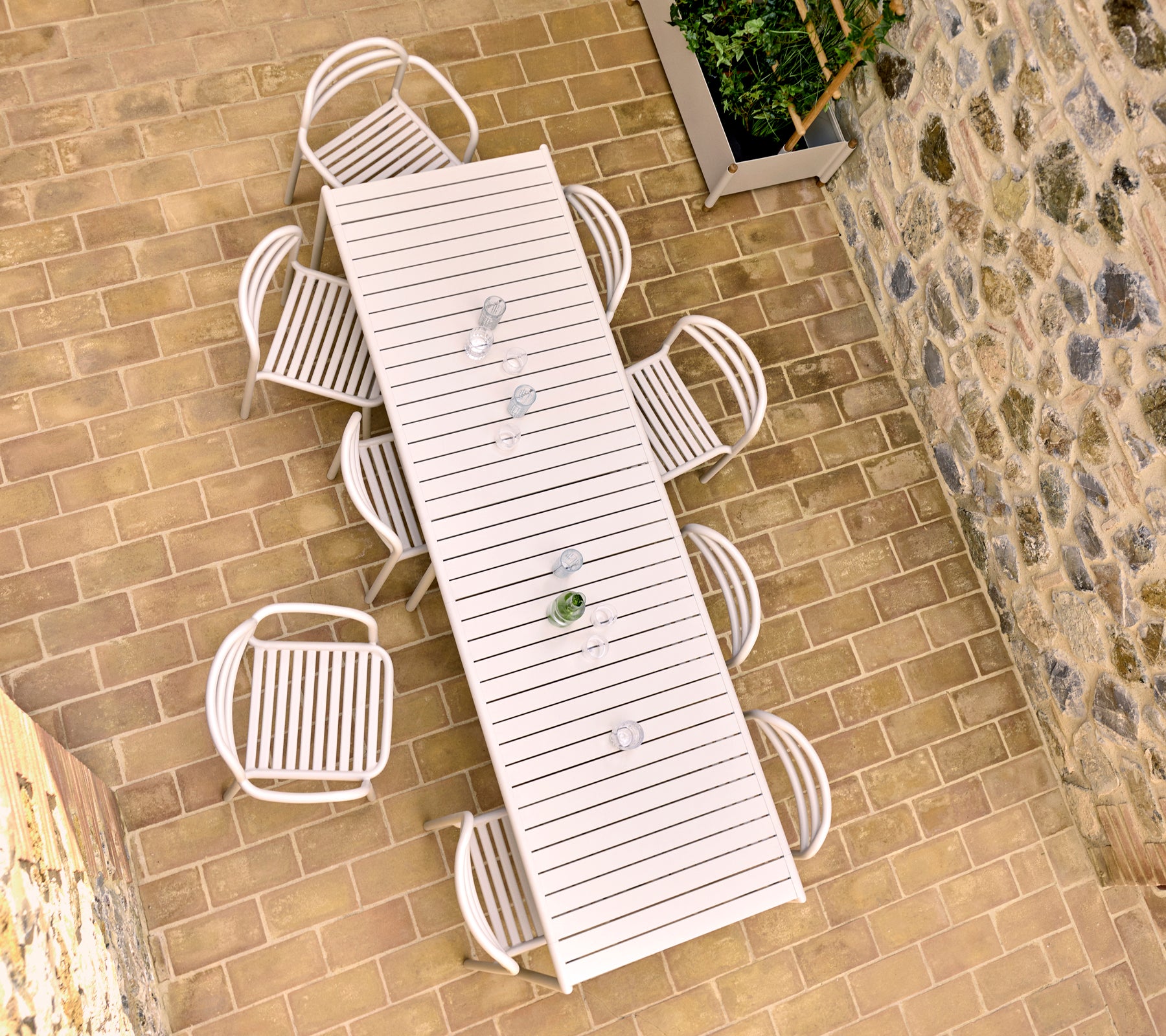 Fugleperspektiv av et sandfarget utemiddagsbord med åtte Bliss-stoler, plassert på en steinlagt terrasse.