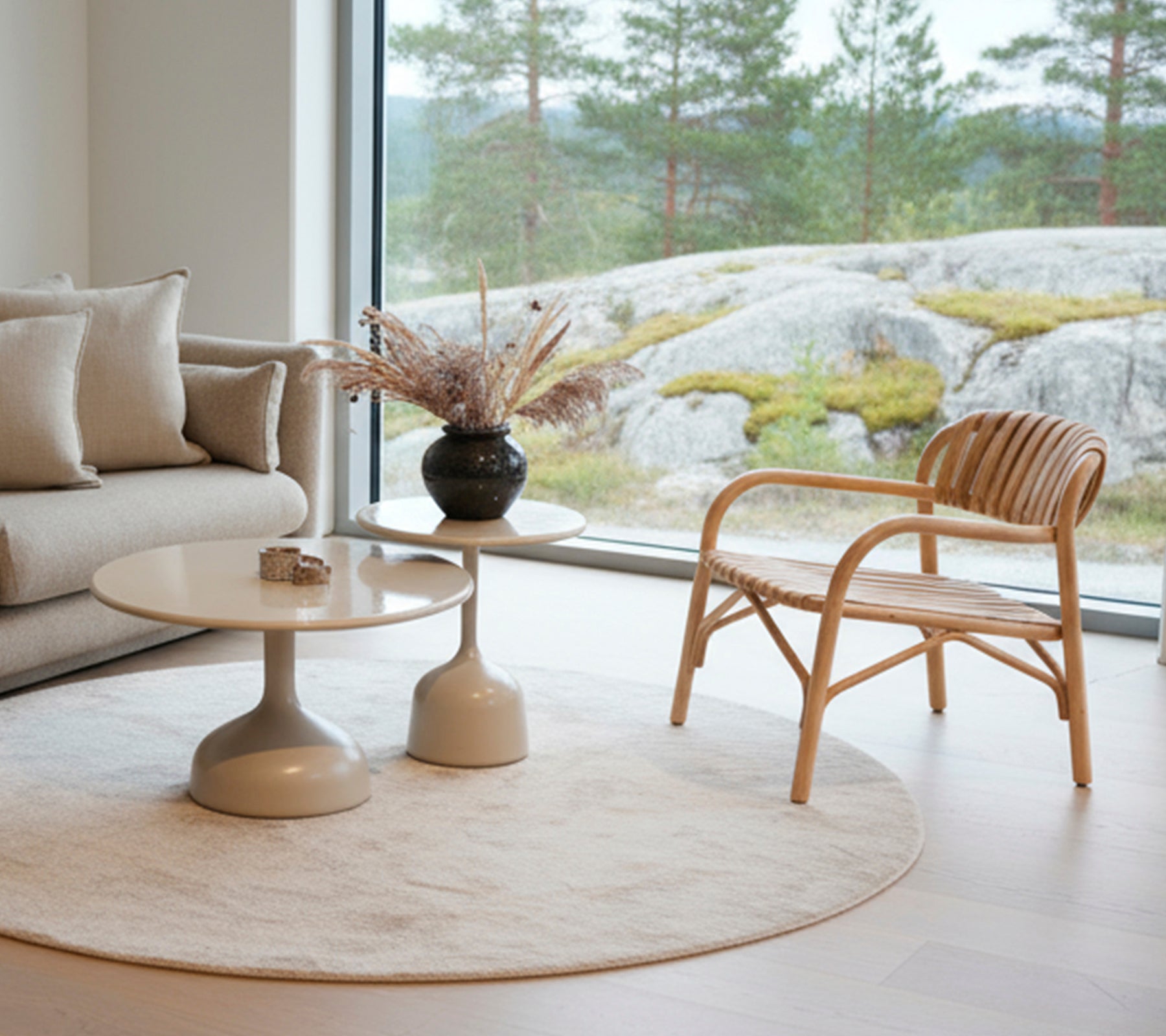 Moderne stue med en sofa, rundt bord, svart vase og rattan stol nær et stort vindu.