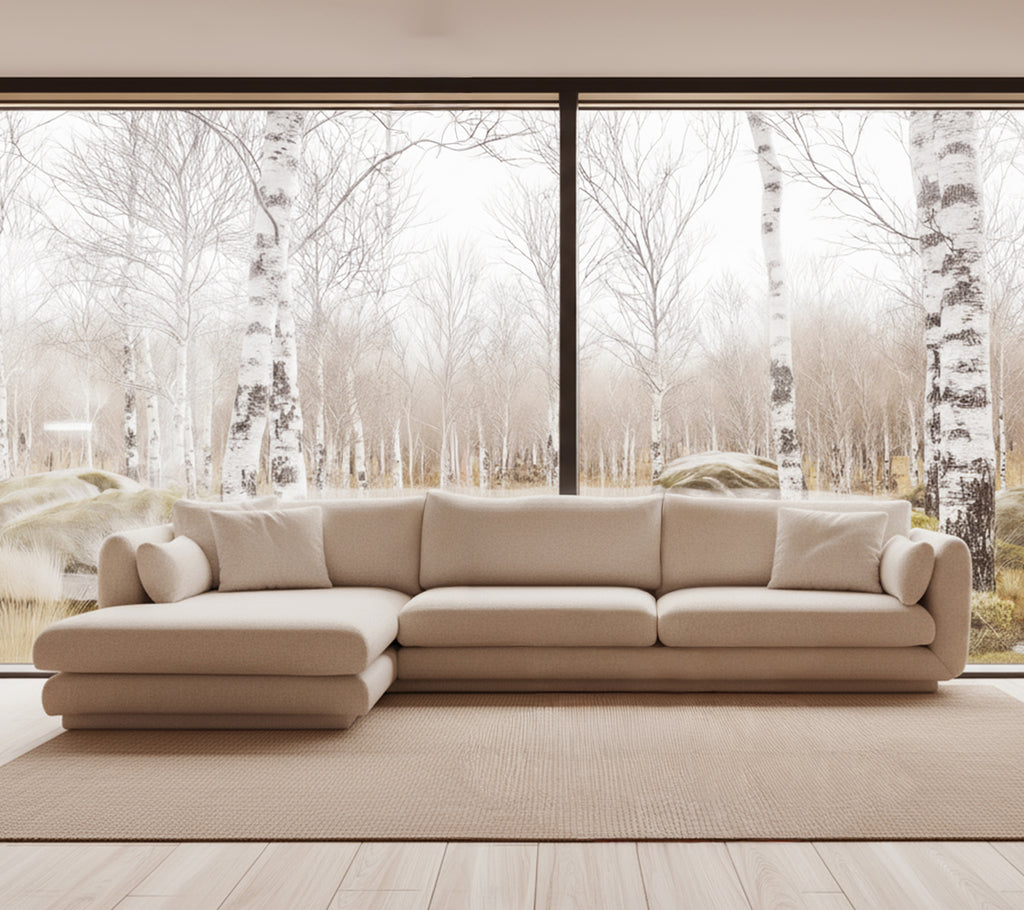 Beige moderne sofa i en lys stueinnredning med store vinduer.