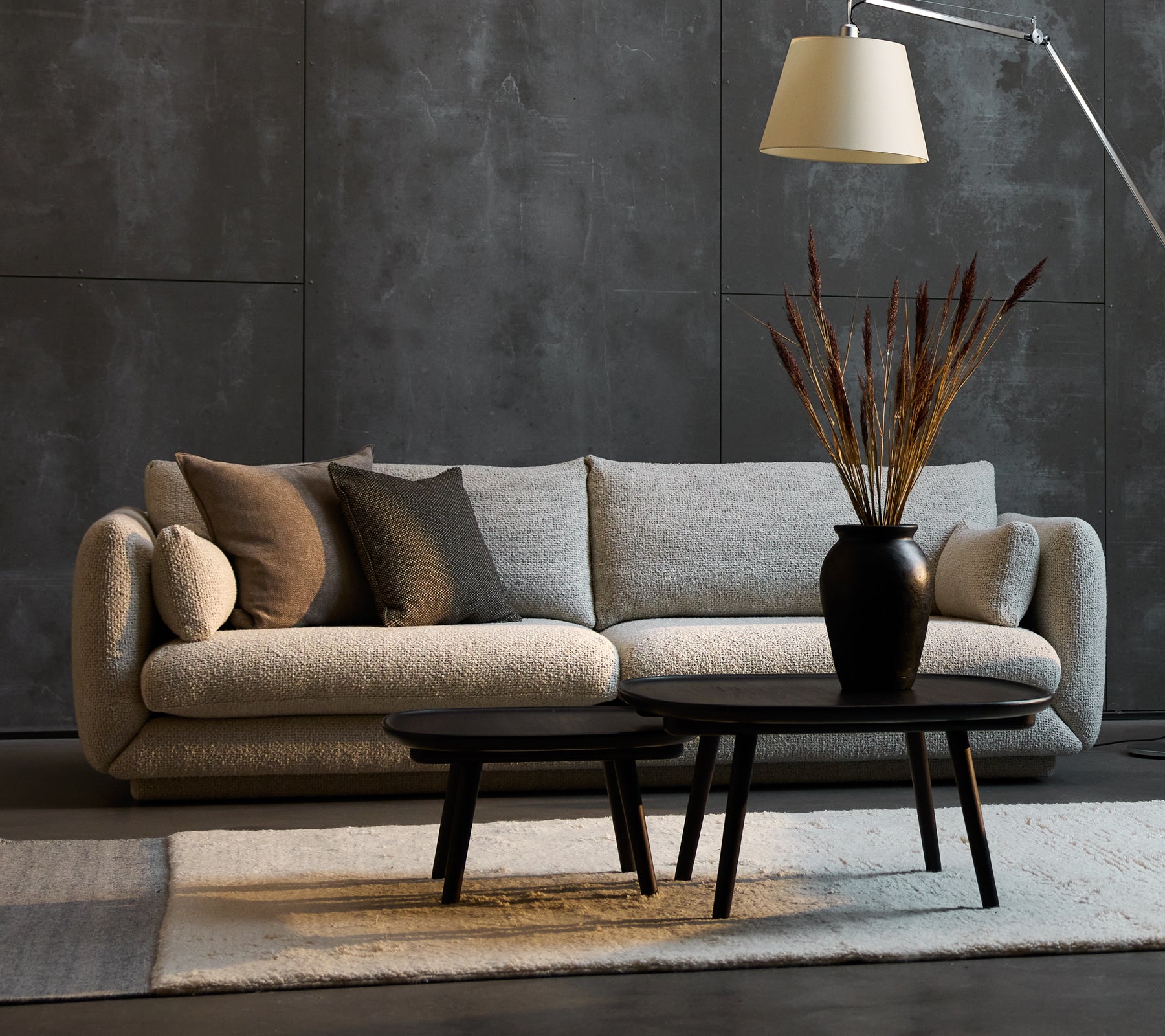 Bloom 3-seters sofa i sandfarge med dekorative puter, ledsaget av to Pace sofabord i forskjellige størrelser og en stilfull gulvlampe.