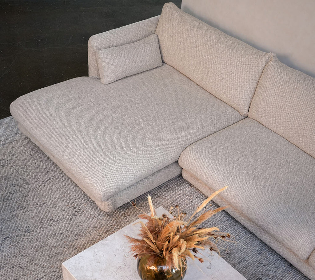 Moderne beige sofa med et hvitt bord og en dekorativ vase i en stilig loungeinnstilling.