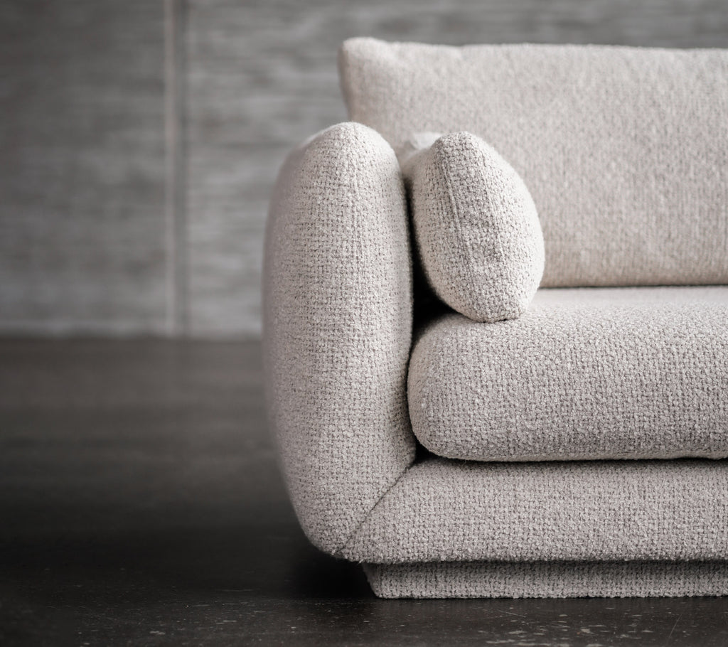 Moderne lysegrå sofa med avrundede armlener og putedetaljer.