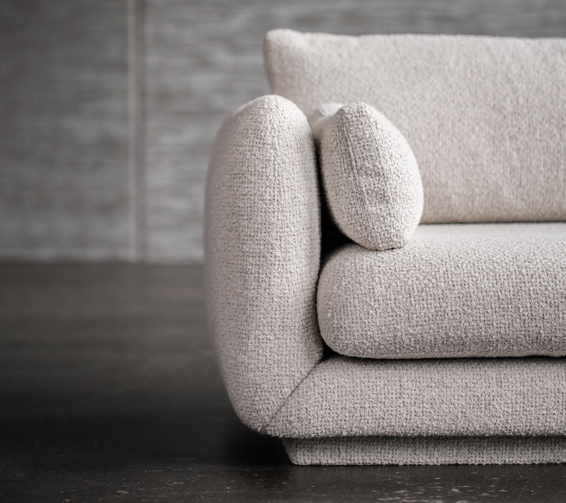 Moderne lysegrå sofa med avrundede armlener og putedetaljer.