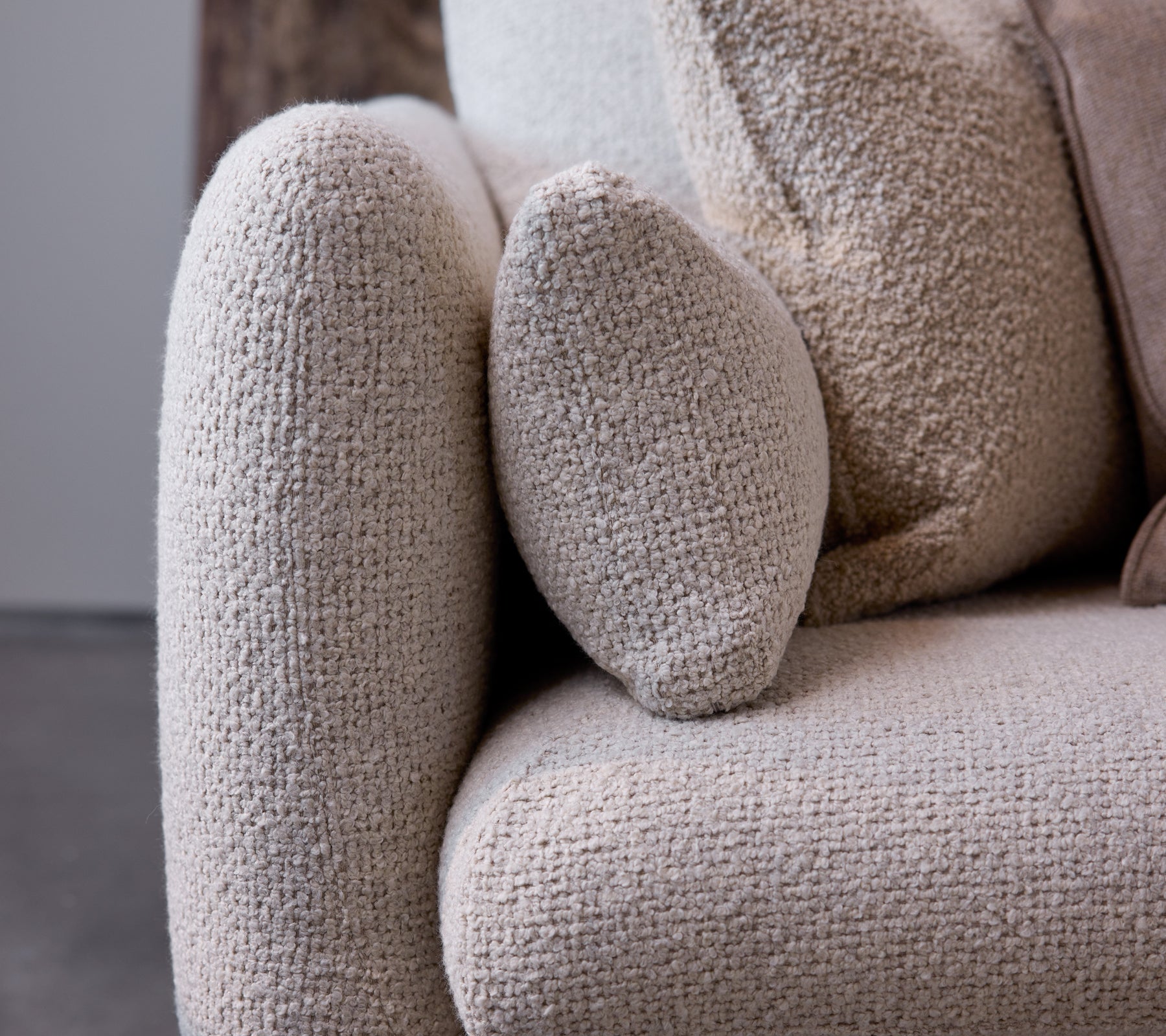  nært bilde av armlenet på en Bloom-sofa i en sandfarge tekstur, som viser et avrundet design og myk, koselig stoff.