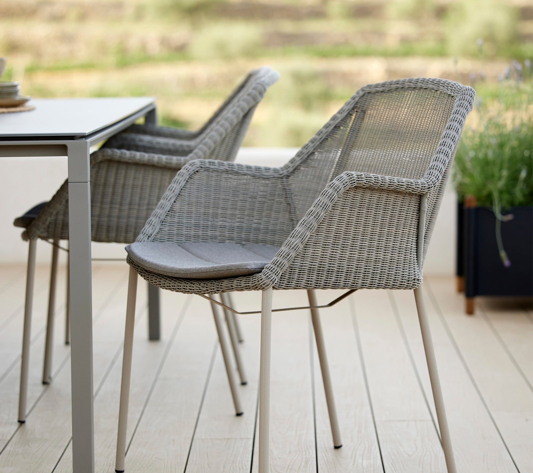 To stilige vevde stoler ved siden av et moderne bord, med en slank design og komfortable puter, ideelt for avslapning i en rolig setting.