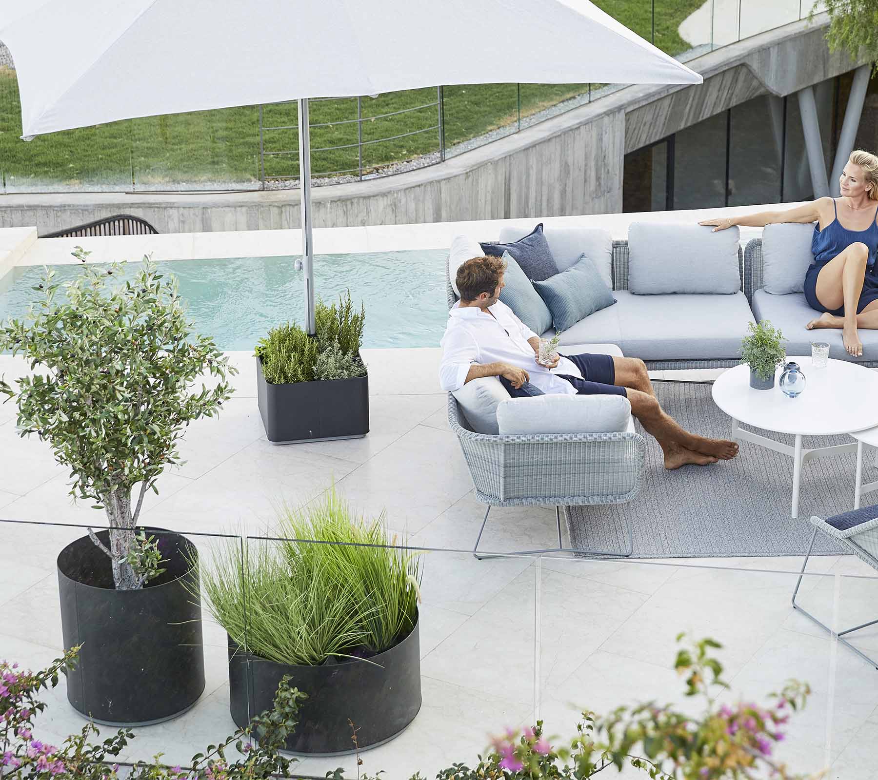 Et stilfullt uteområde med en komfortabel sofa, planter og et stort parasoll, perfekt for avslapning.