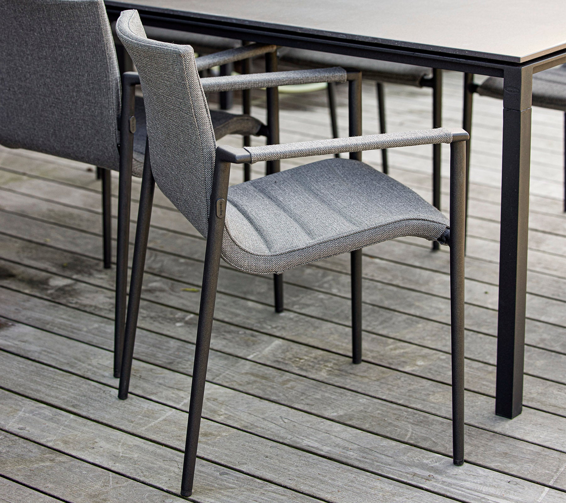 Stilig grå stol med armlener plassert ved siden av et elegant svart bord på en trebordflate. Ideell for moderne utendørsomgivelser.