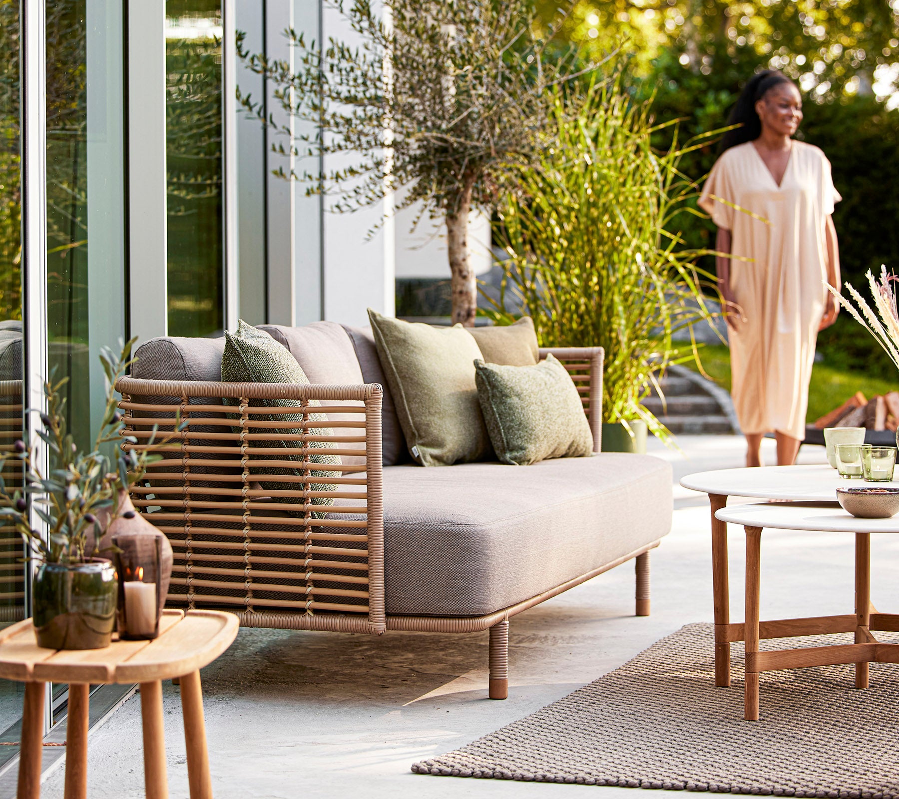 Et koselig sitteområde med en lys sofa, grønne puter, dekorative planter og et trebord, som skaper en innbydende atmosfære.