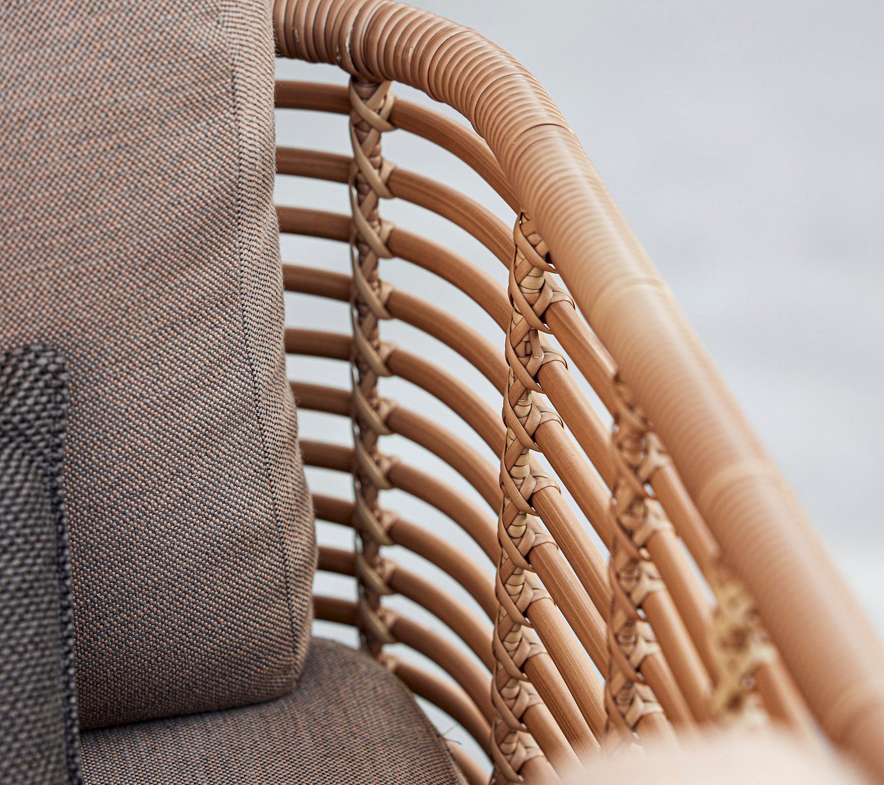 Nærbilde av en stilfull lenestol med flettede rattan-detaljer og myke puter i nøytrale farger, som viser frem moderne design.