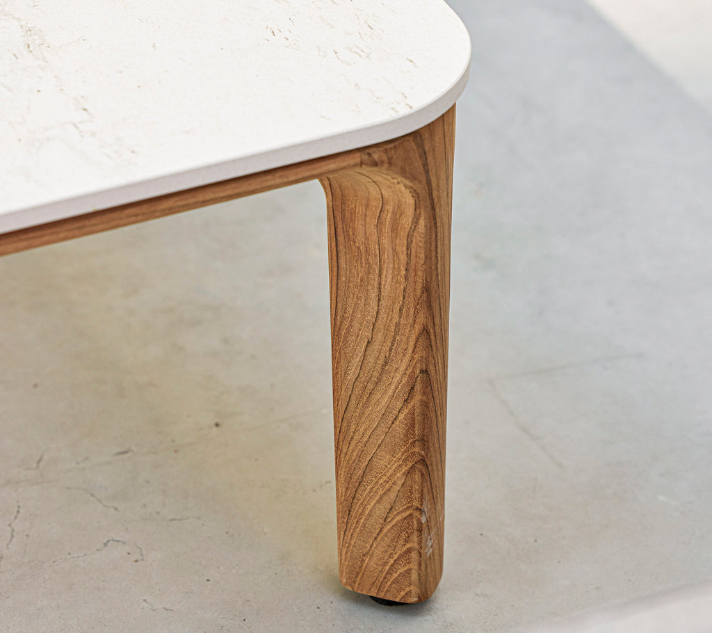 Et nærbilde av et bord med et teksturert trebein og en glatt, hvit bordplate. Elegante og moderne designelementer fremheves.