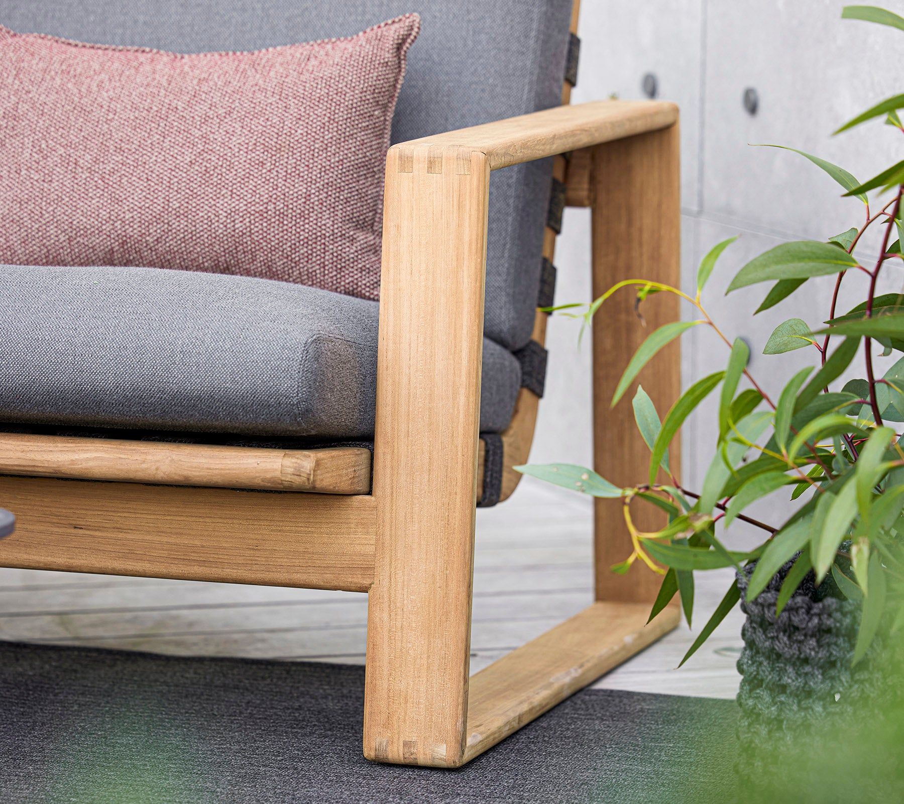 en moderne sofa med en trelast, som har grå puter og en dekorativ pute, supplert av frodige grønne planter i nærheten.