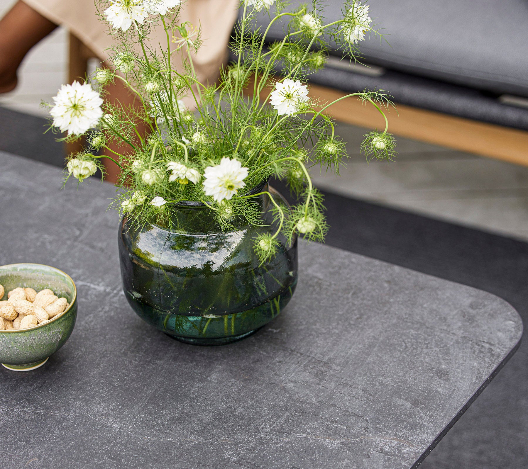 Et moderne bord med en rund glassvase med hvite blomster og en liten skål med nøtter. Overflaten er glatt og teksturert.