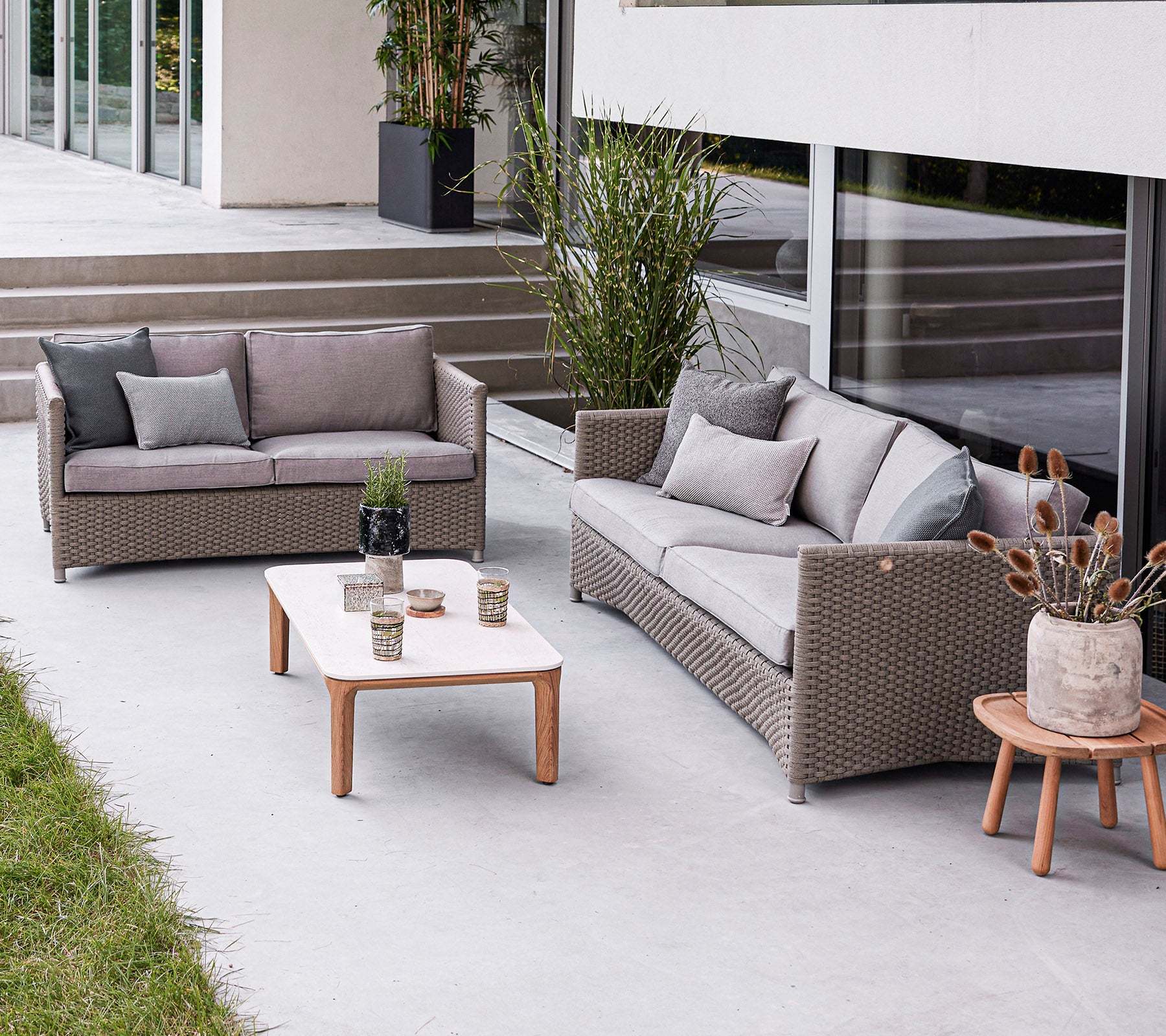 Moderne utendørs sittegruppe med en sofa, en kjærlighetssofa og et kaffebord med dekorative elementer. Stilfull og innbydende atmosfære.