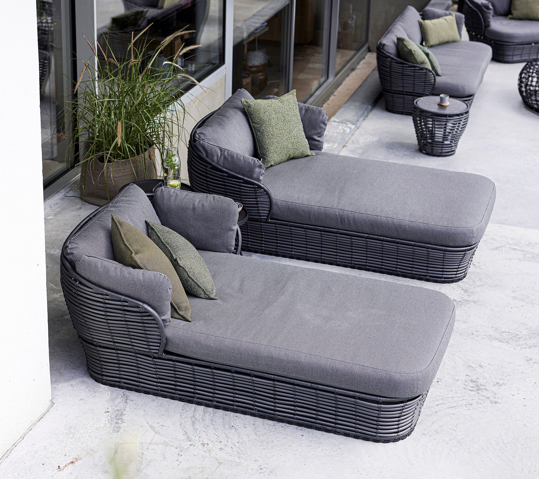 To moderne lounge-stoler med myke grå puter og grønne dekorative puter, ledsaget av et rundt sidebord.