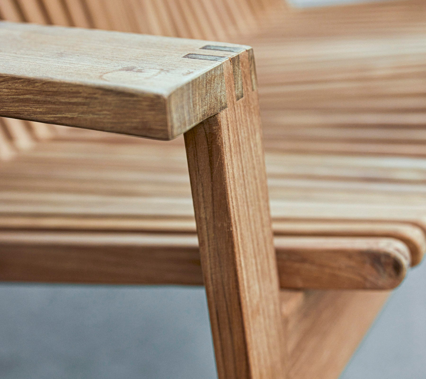Nærbilde av en armlene på en trebark stol som viser et stilrent design med lamellert seter og glatte overflater.