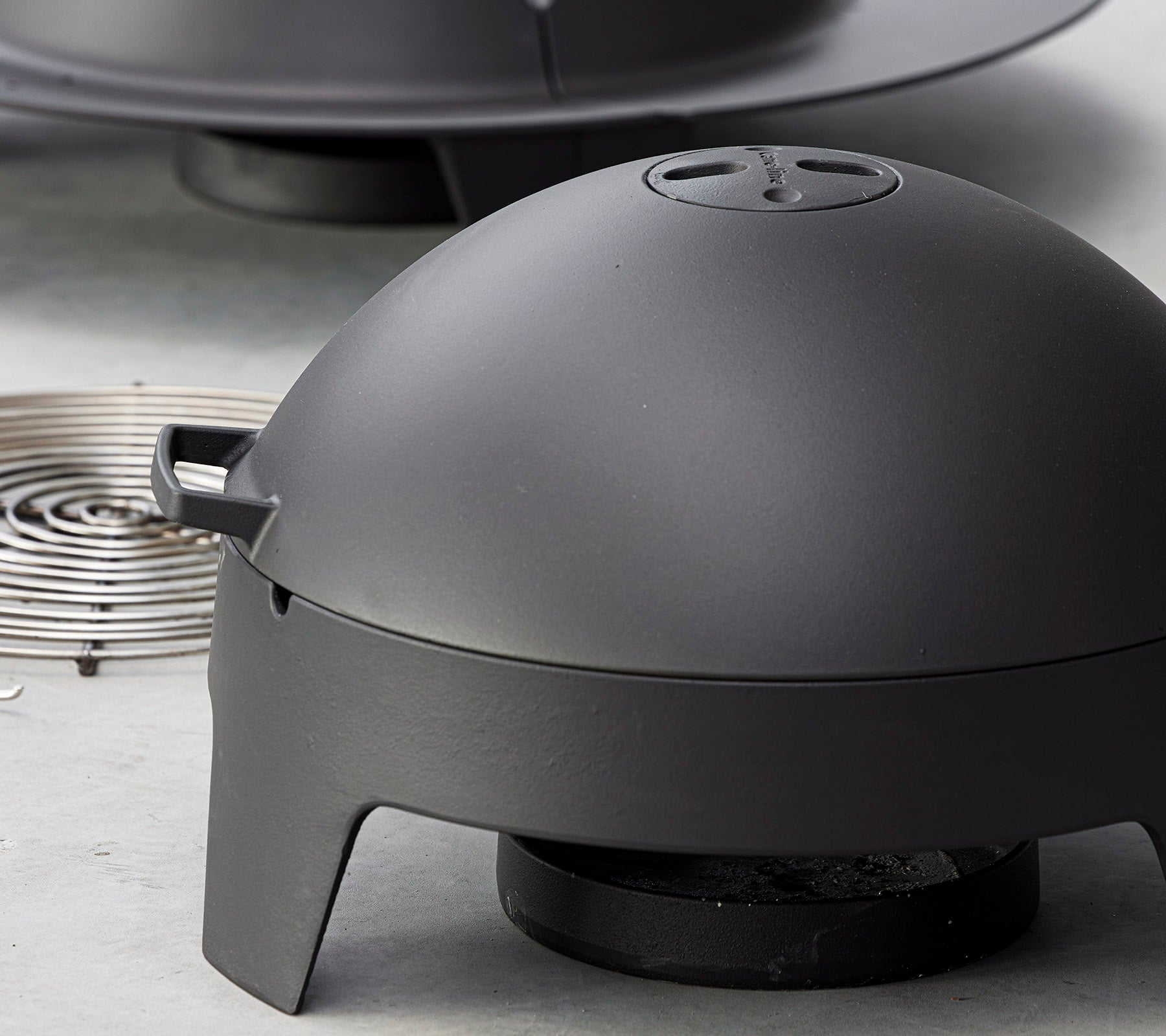 Matt svart kokeapparat med et kuppelformet lokk og en avtakbar varmekilde, designet for utegrilling og grilling.