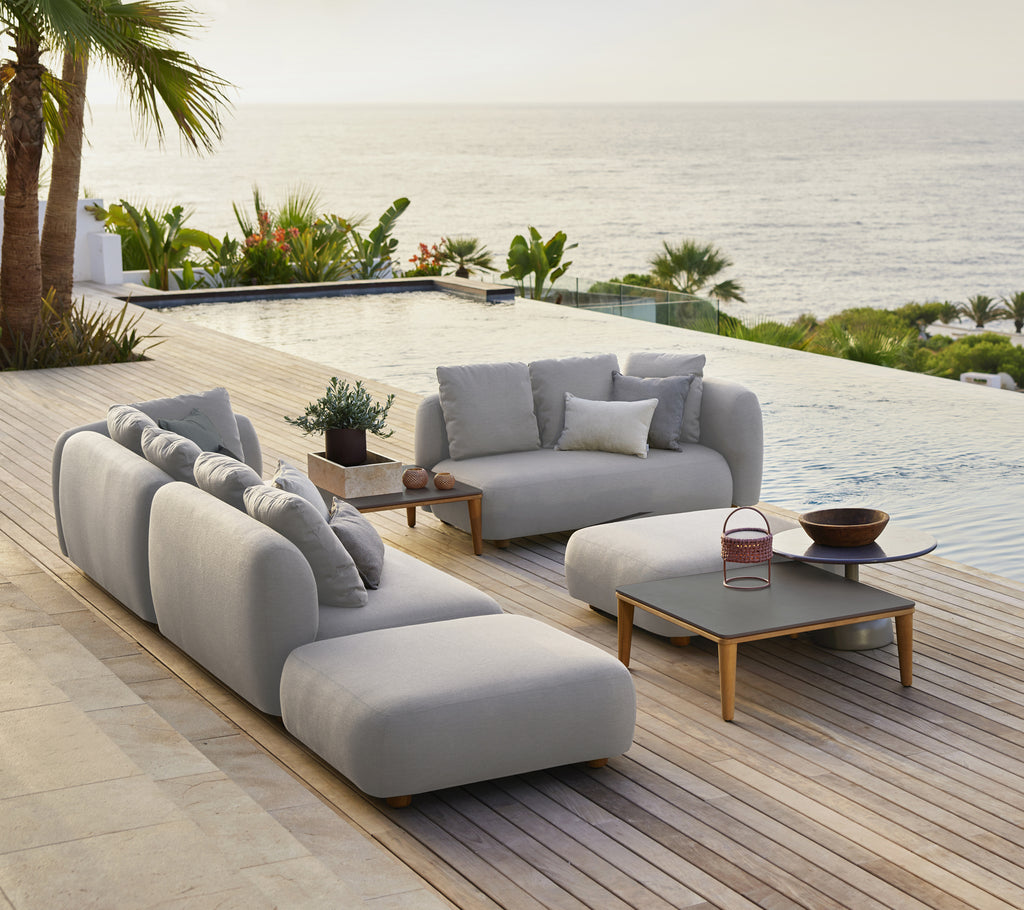 Stilig grå sofa med puter og et svart kaffebord i en moderne ute-lounge ved havet.