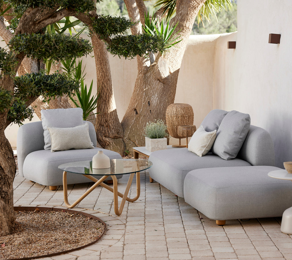 Moderne grå sofa og stol med et glassbord i et stilrent uteområde.