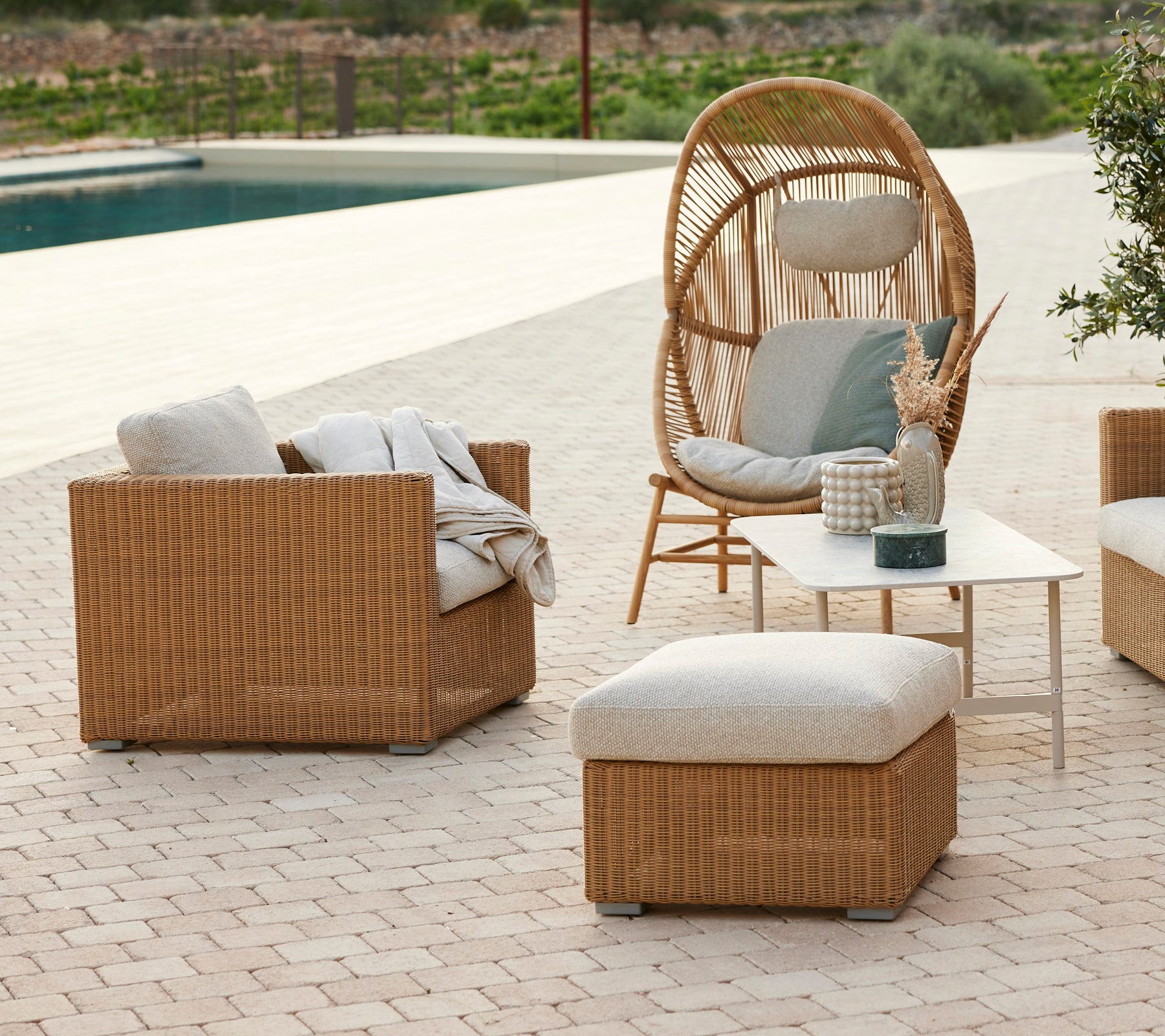 Moderne loungeområde med en rattan stol, grå puter, rattan sofa og et salongbord.