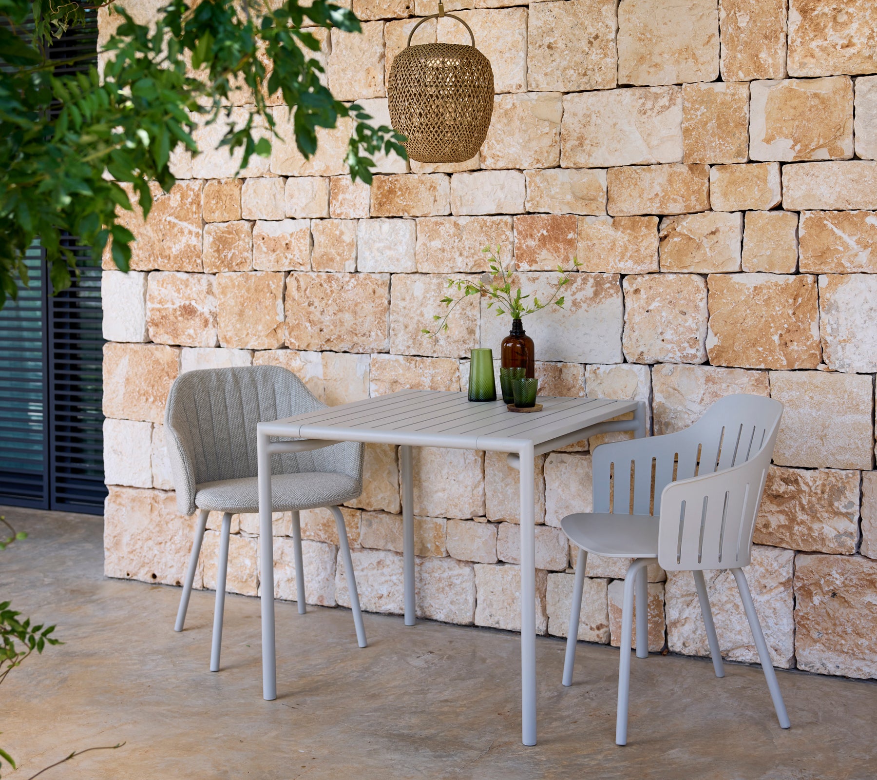 Moderne grå bord og stoler med grønne og brune flasker i en utendørs setting.