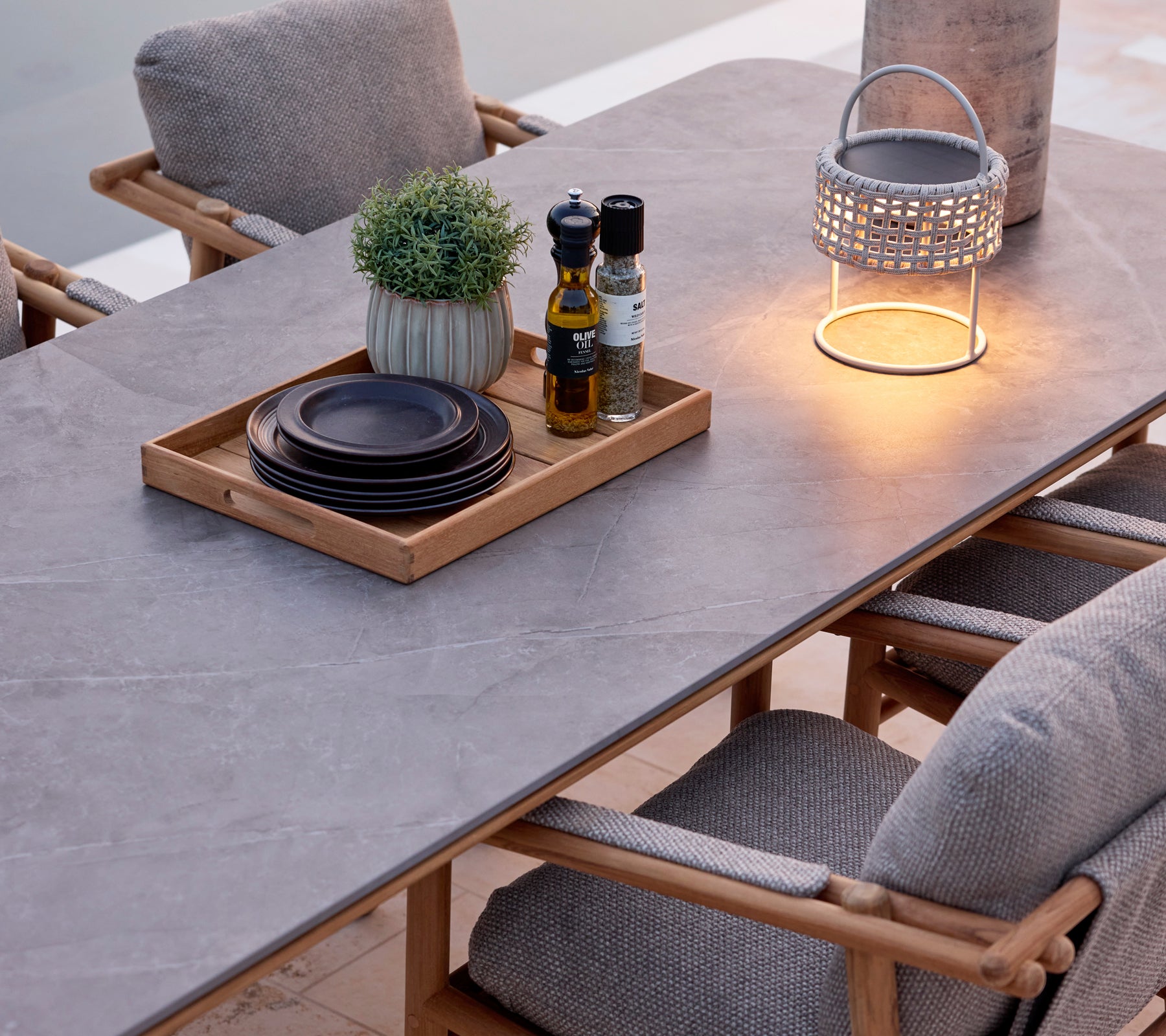 Moderne spisebord med grå overflate, brune stoler, svarte tallerkener og en dekorativ lampe.