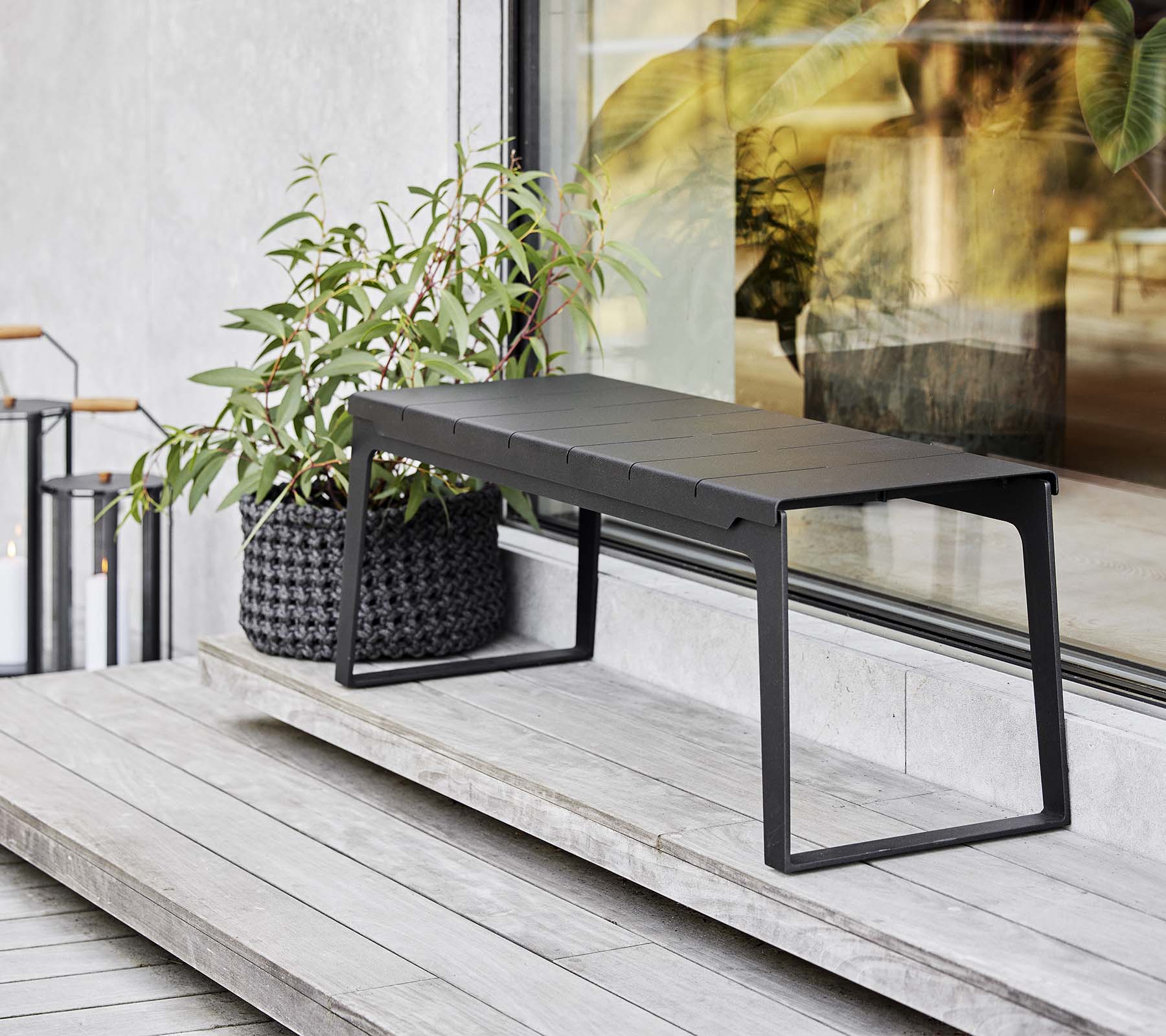 En slank svart benk plassert ved siden av en plantekasse med grønt, som viser moderne designelementer og minimalisme.