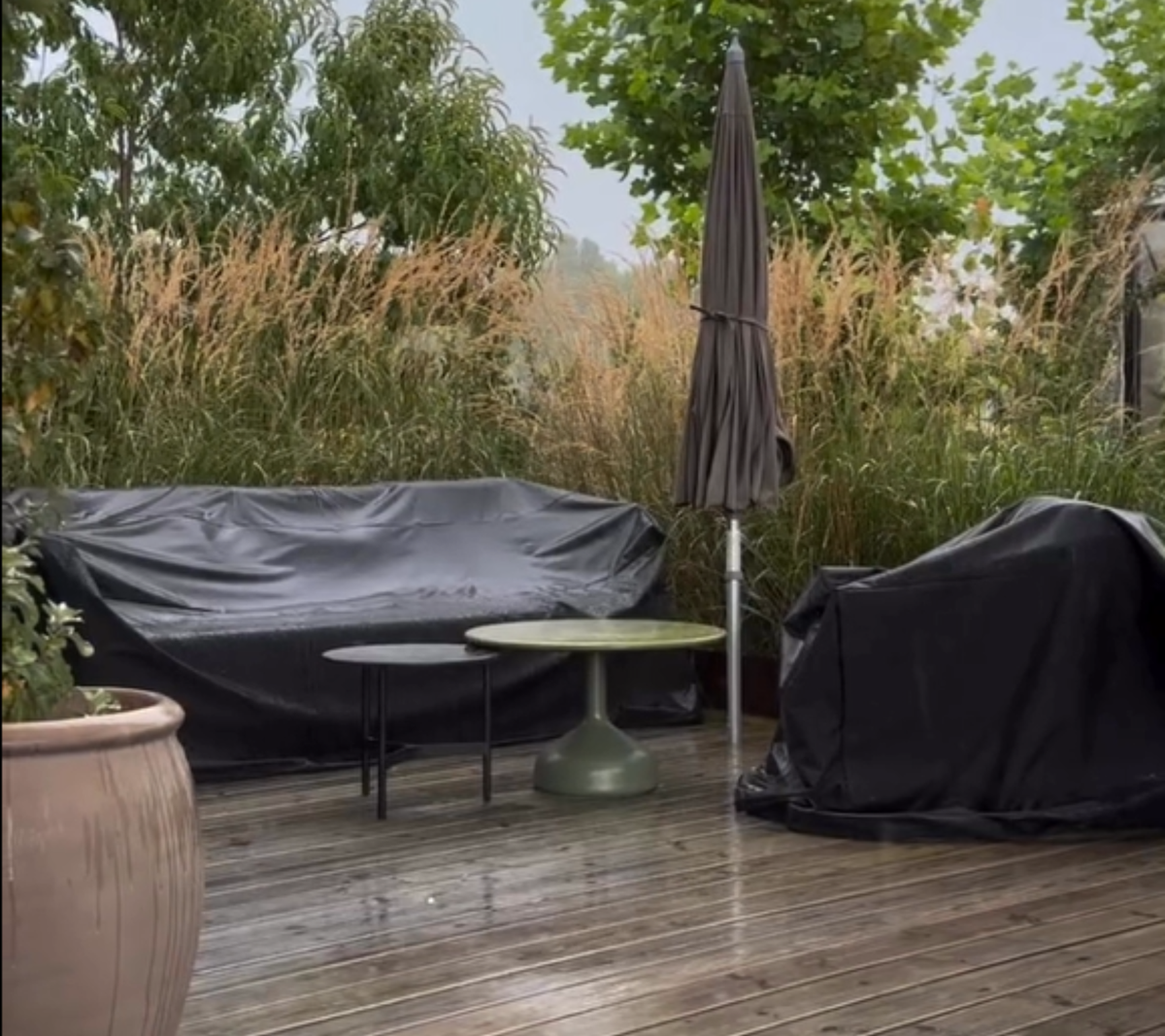 Uteområde med svart sofa, grønt bord og svart stol omgitt av grønne planter.